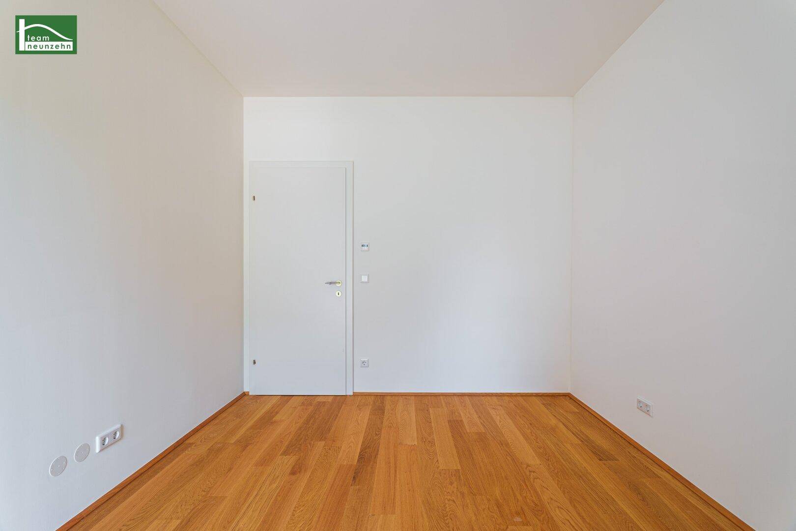 Leerer Raum mit Holzboden und einer schlichten weißen Tür, bereit für individuelle Gestaltung.
