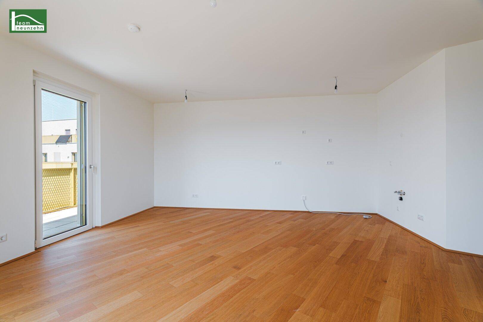 Geräumiger Wohnbereich mit hellem Holzboden und Zugang zu einem Balkon.