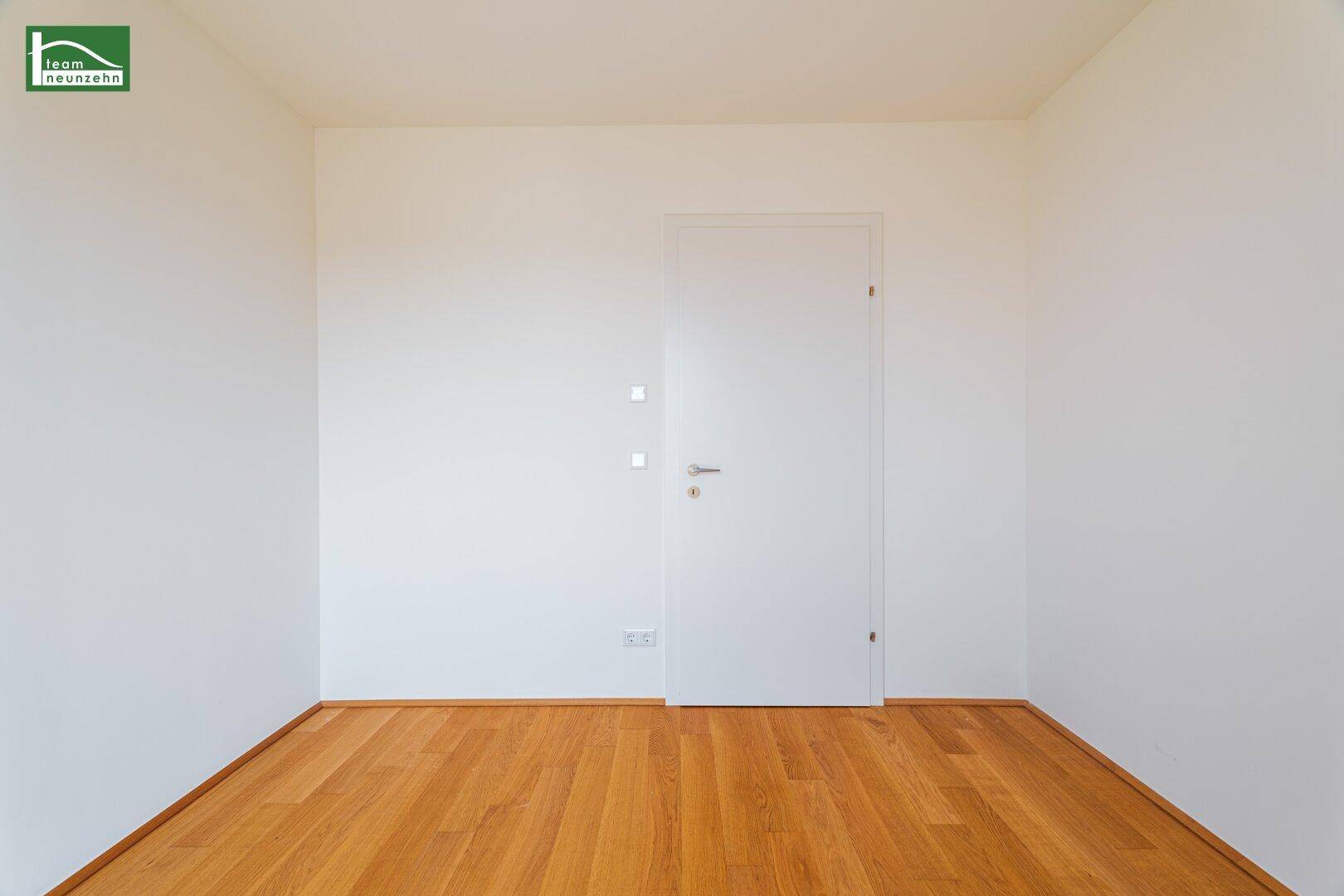 Leeres Zimmer mit Holzboden und weißer Tür, bereit zur individuellen Gestaltung.