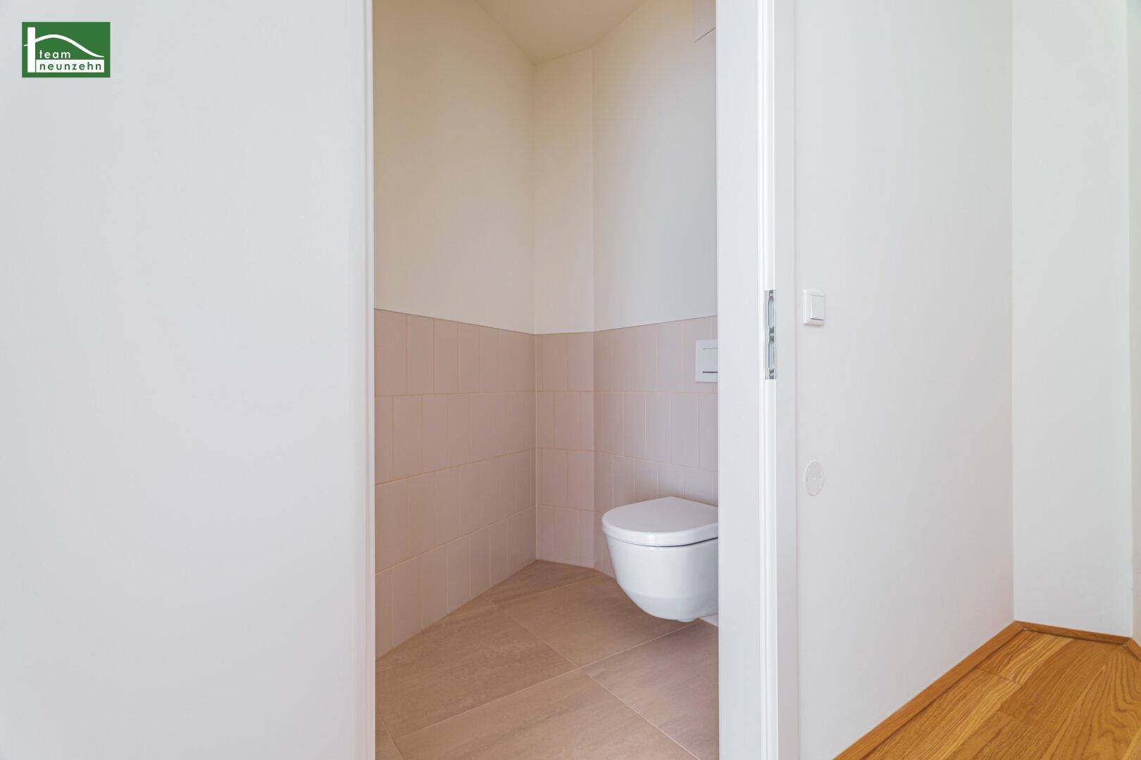Separate Toilette mit Wand-WC und hellen Fliesen, praktisch und funktional.