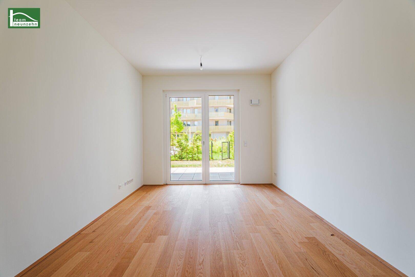 Geräumiger, heller Raum mit Holzboden und großen Glastüren, die viel Tageslicht hereinlassen.