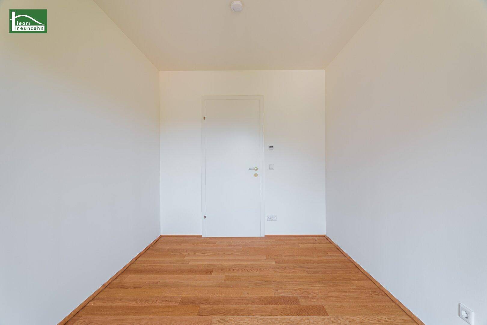 Leeres Zimmer mit Holzboden und einer geschlossenen Tür, bereit für neue Bewohner.