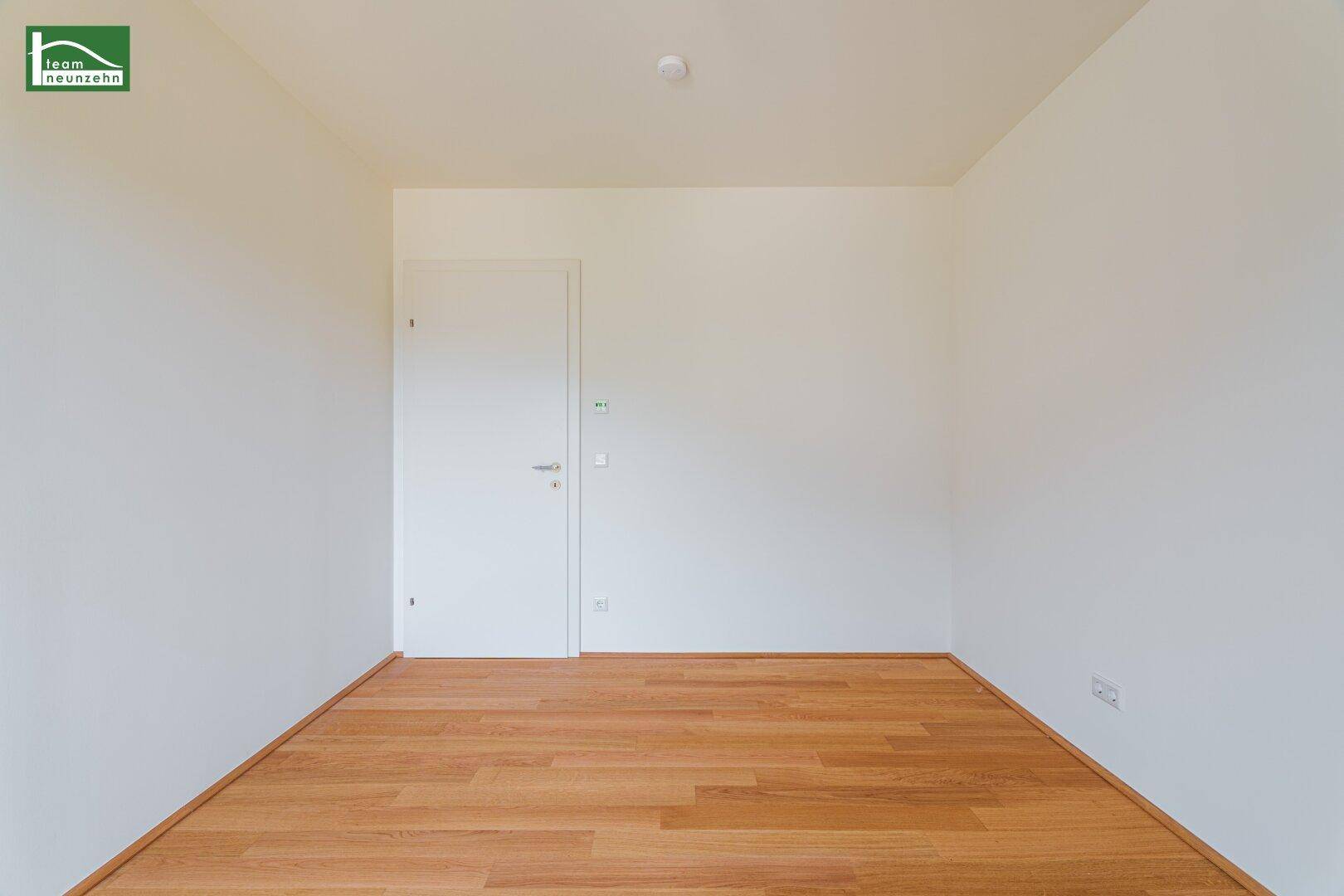 Unmöbliertes Zimmer mit Holzboden und einer weißen Tür, bereit zur individuellen Gestaltung.