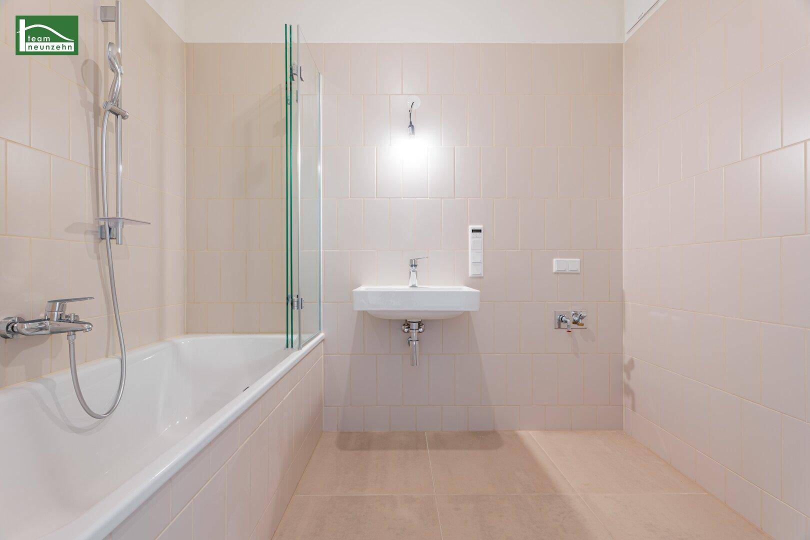 Modernes Badezimmer mit Badewanne, Duschabtrennung und Waschbecken in hellen Fliesen.