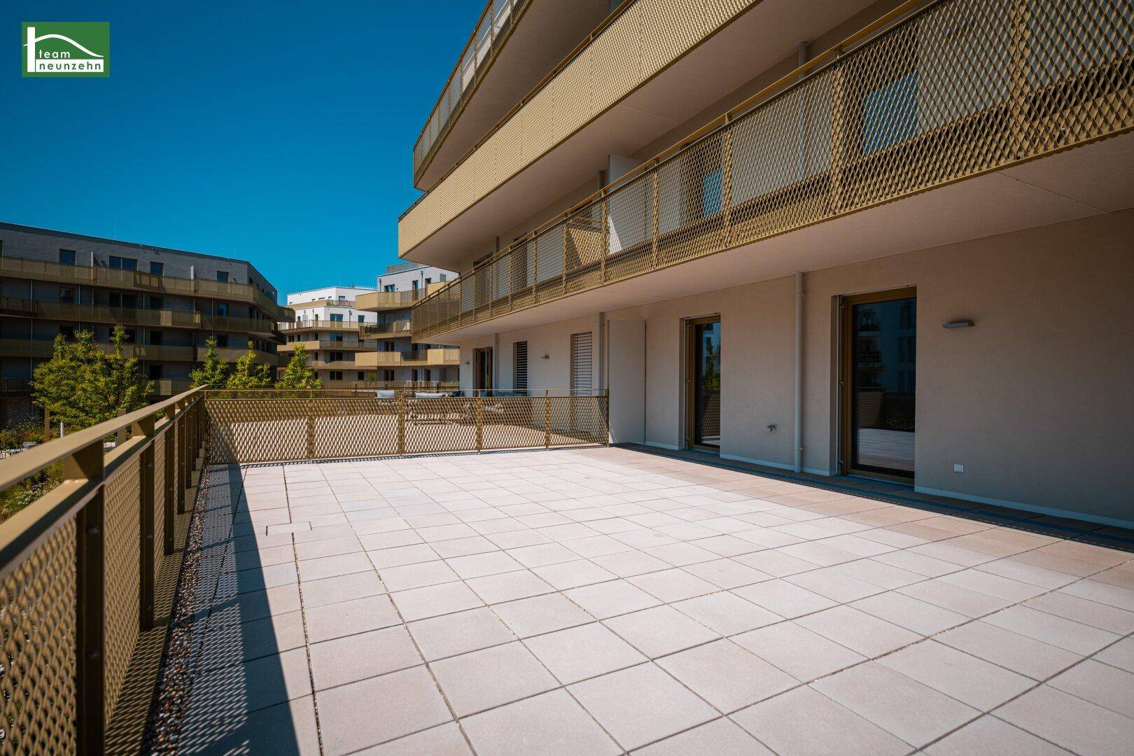 Große, sonnige Terrasse mit Fliesenboden und Blick auf die umliegenden Gebäude.