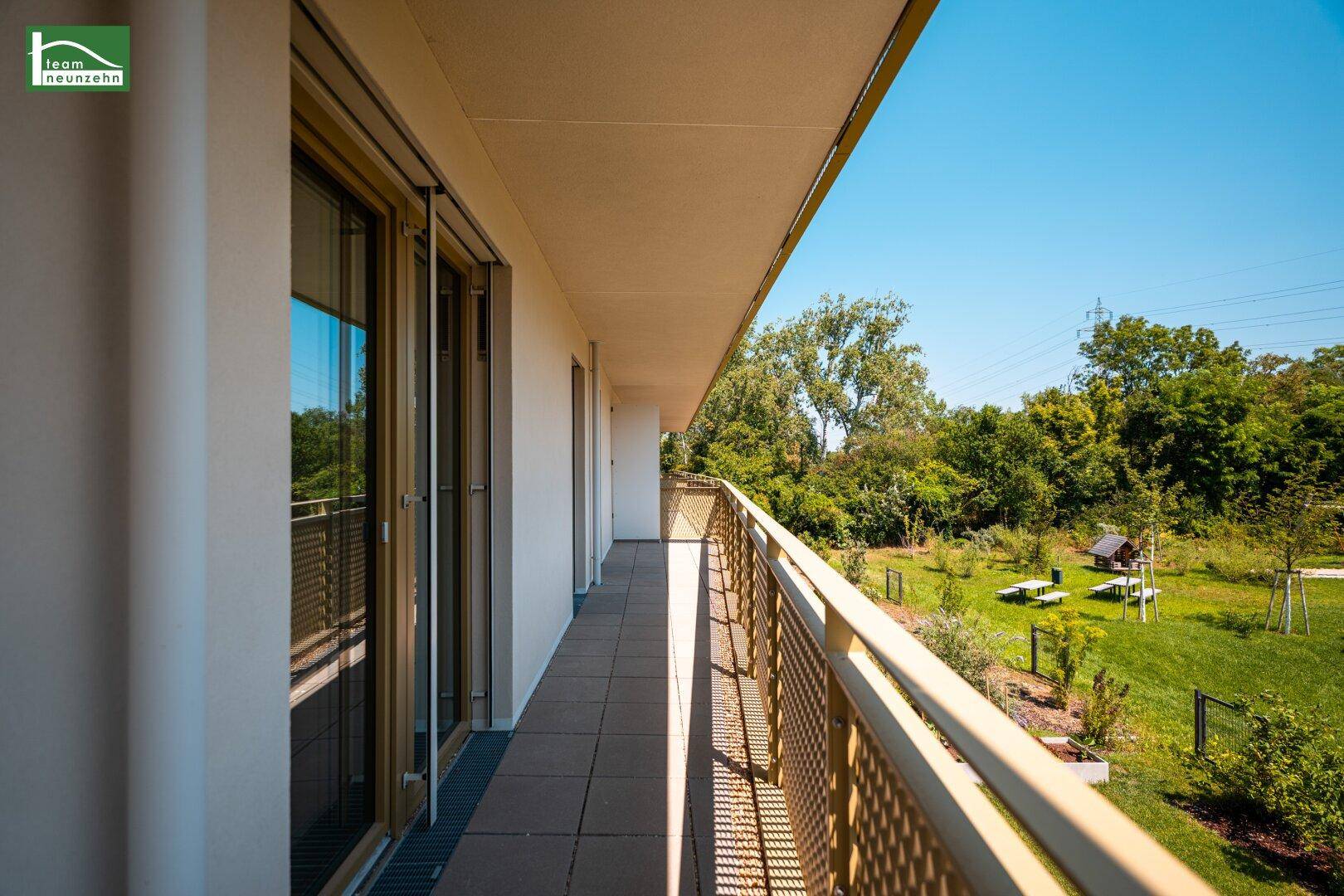 Langer Balkon mit Gittergeländer und Blick auf eine grüne Parkanlage.
