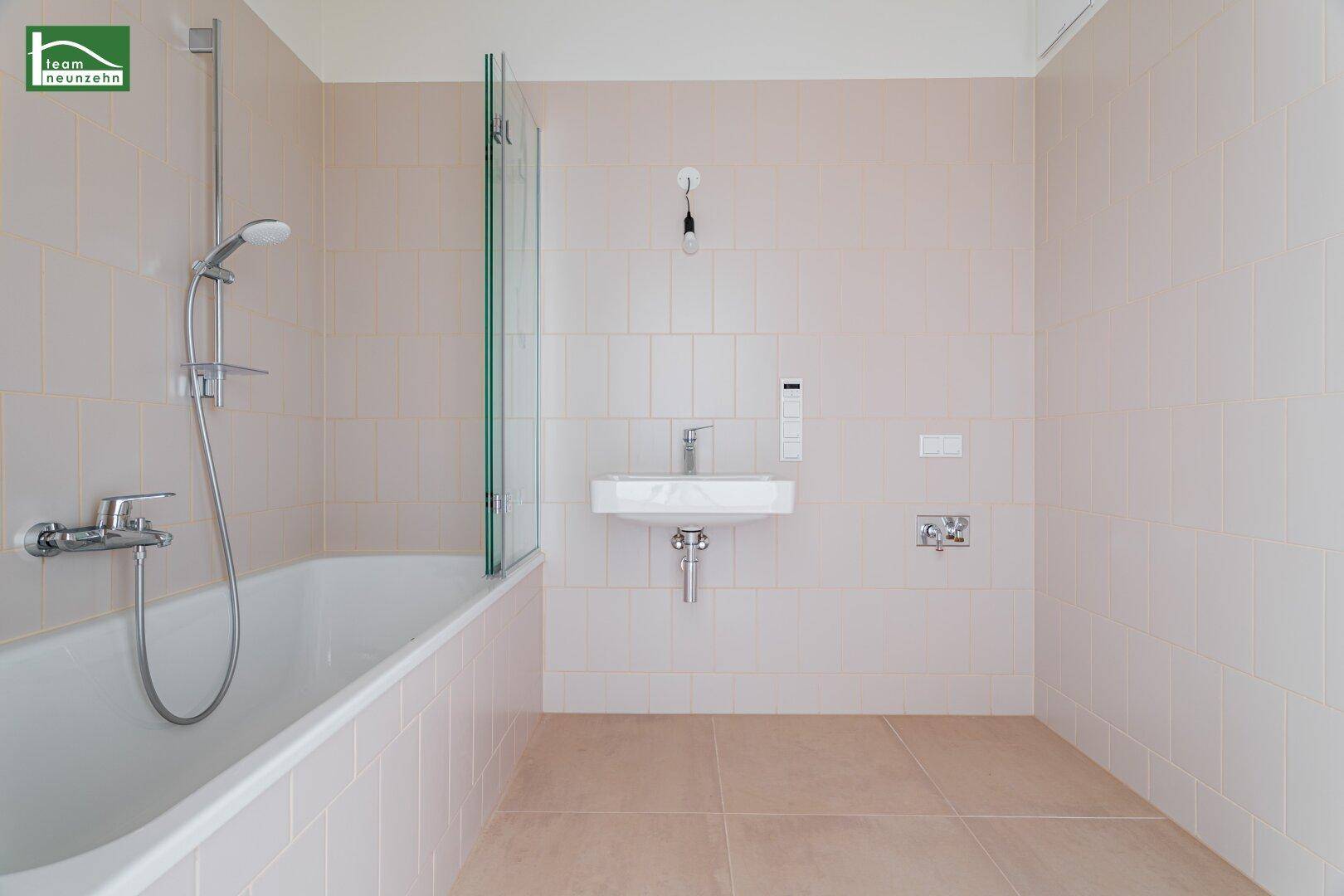 Modernes Badezimmer mit hellbeigen Fliesen, Badewanne mit Duschfunktion und einem Waschbecken.