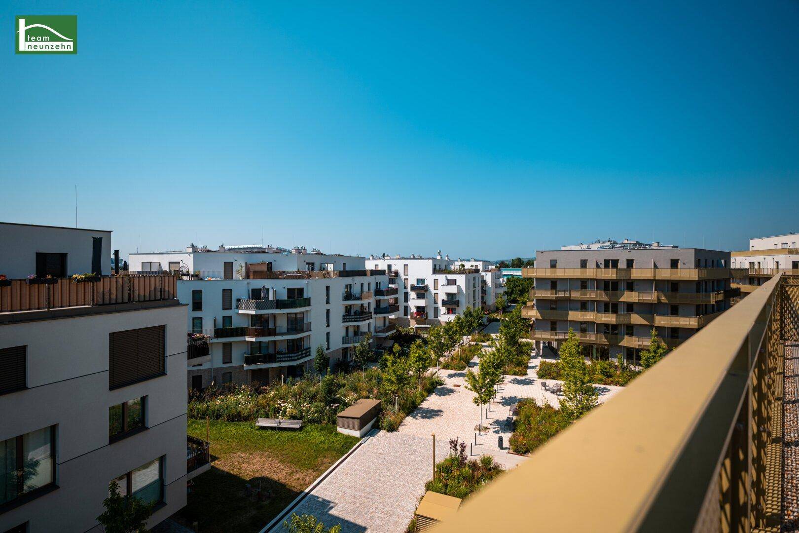 Weitläufiger Blick von einem Balkon auf eine moderne Wohnanlage mit Grünflächen und Wegen.