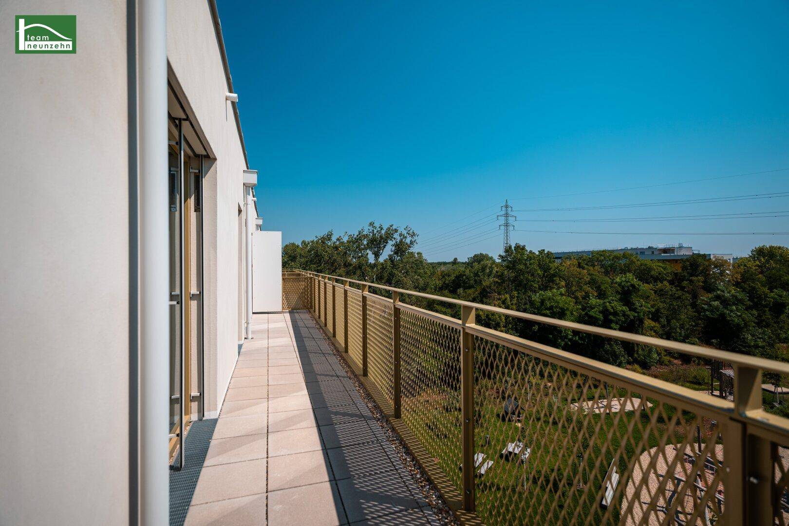 Langer Balkon mit Fliesenboden und gelbem Metallgeländer, bietet einen Blick ins Grüne.