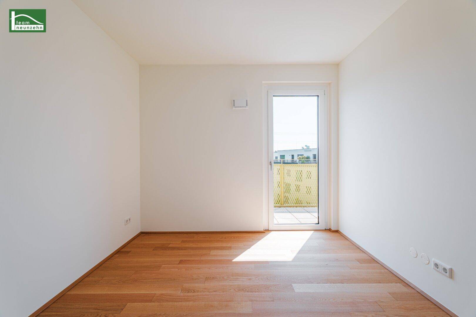 Freundliches Zimmer mit Holzboden und Zugang zu einem Balkon, das von der Sonne durchflutet wird.