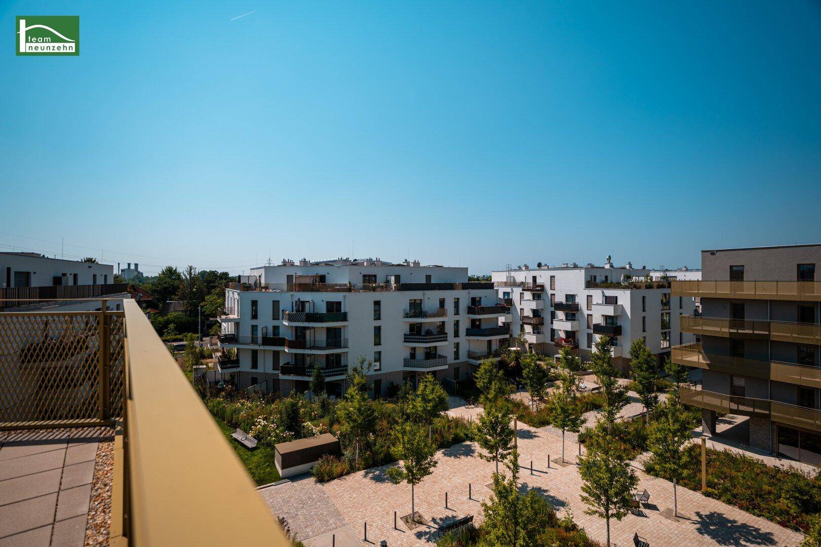 Panoramablick auf eine moderne Wohnsiedlung mit viel Grün und klarem Himmel.