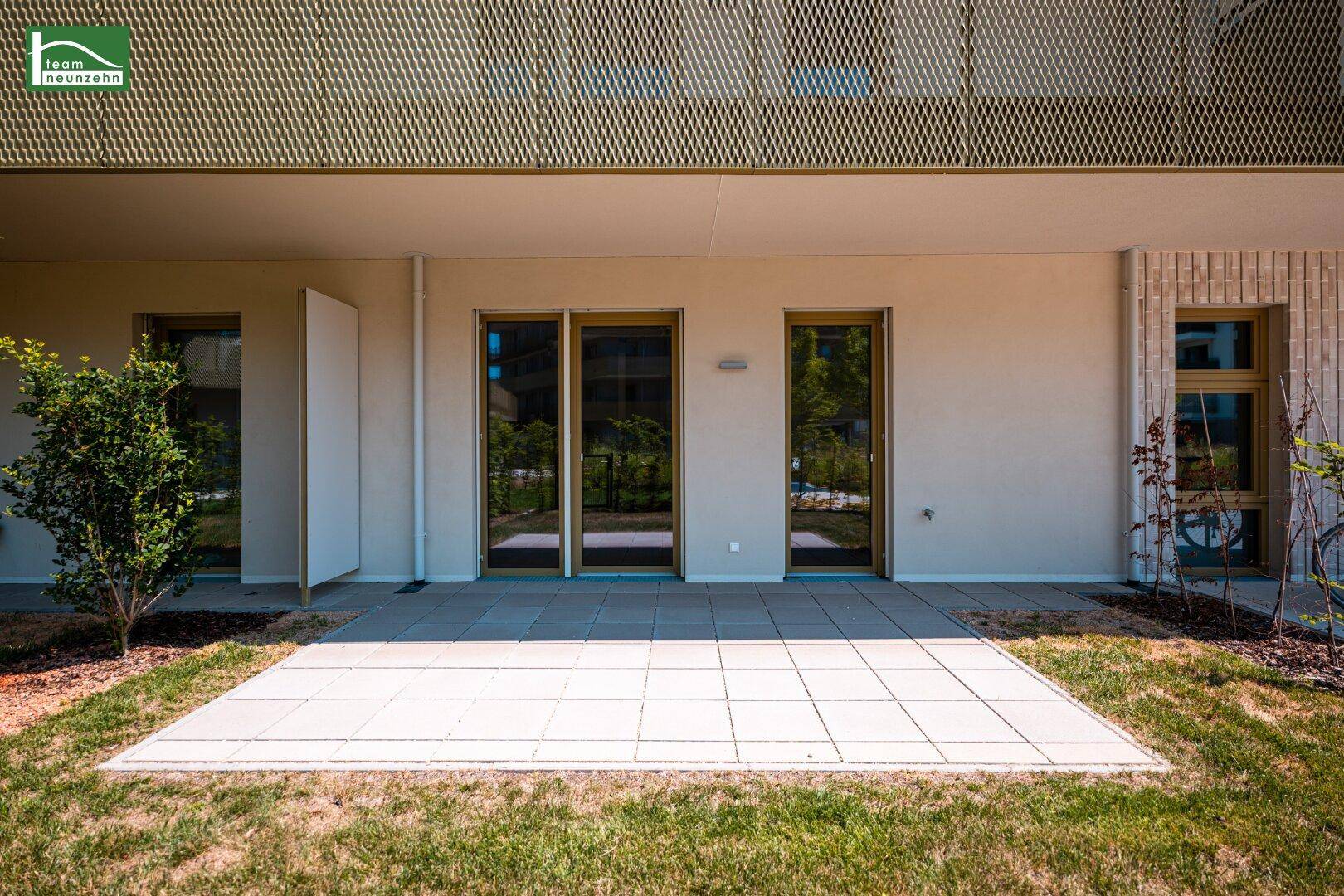 Großzügige Terrasse mit Steinplatten und angrenzendem Rasenbereich vor moderner Fassade.