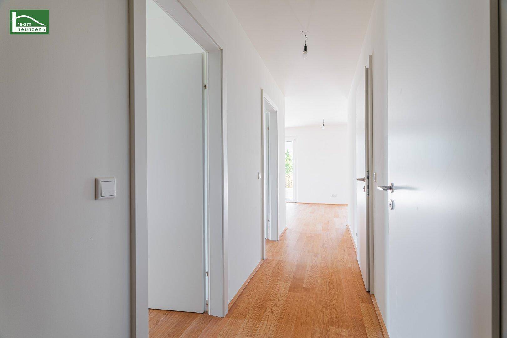 Heller Flur mit Holzboden und mehreren weißen Türen, der verschiedene Räume verbindet.