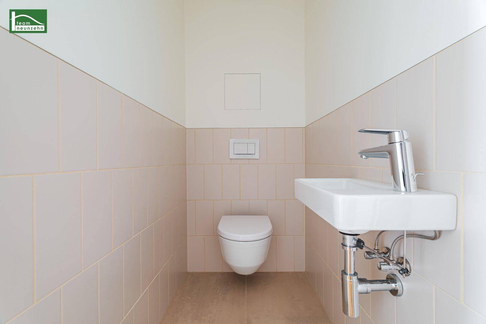Modernes Gäste-WC mit wandhängender Toilette und kleinem Waschbecken, in hellen Beigetönen gefliest.