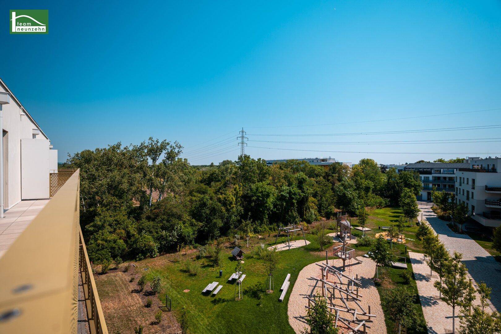 Balkon mit weitem Blick auf einen Spielplatz und eine grüne Parklandschaft.