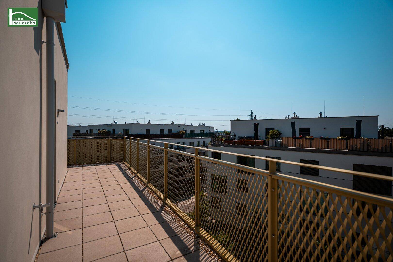 Langer Balkon mit modernen Geländern und Ausblick auf weitere Neubauten in der Umgebung.