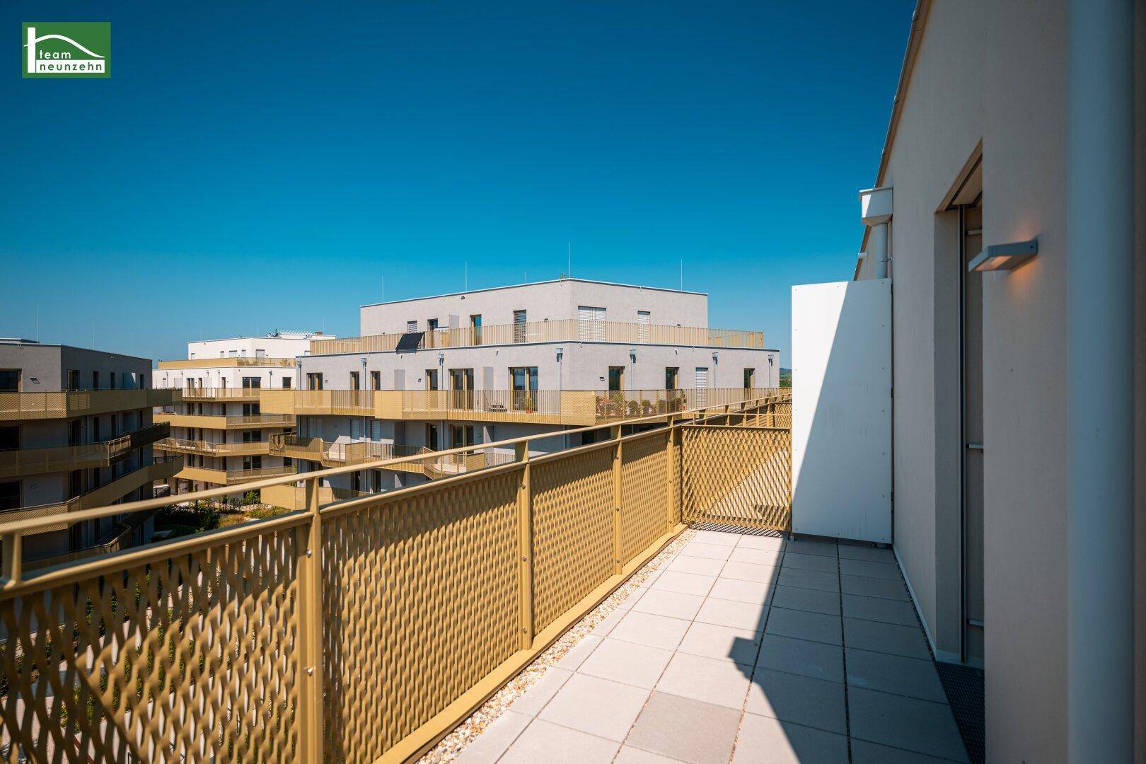 Sonniger Balkon mit moderner Brüstung und Ausblick auf die Nachbarschaft und weitere Gebäude.