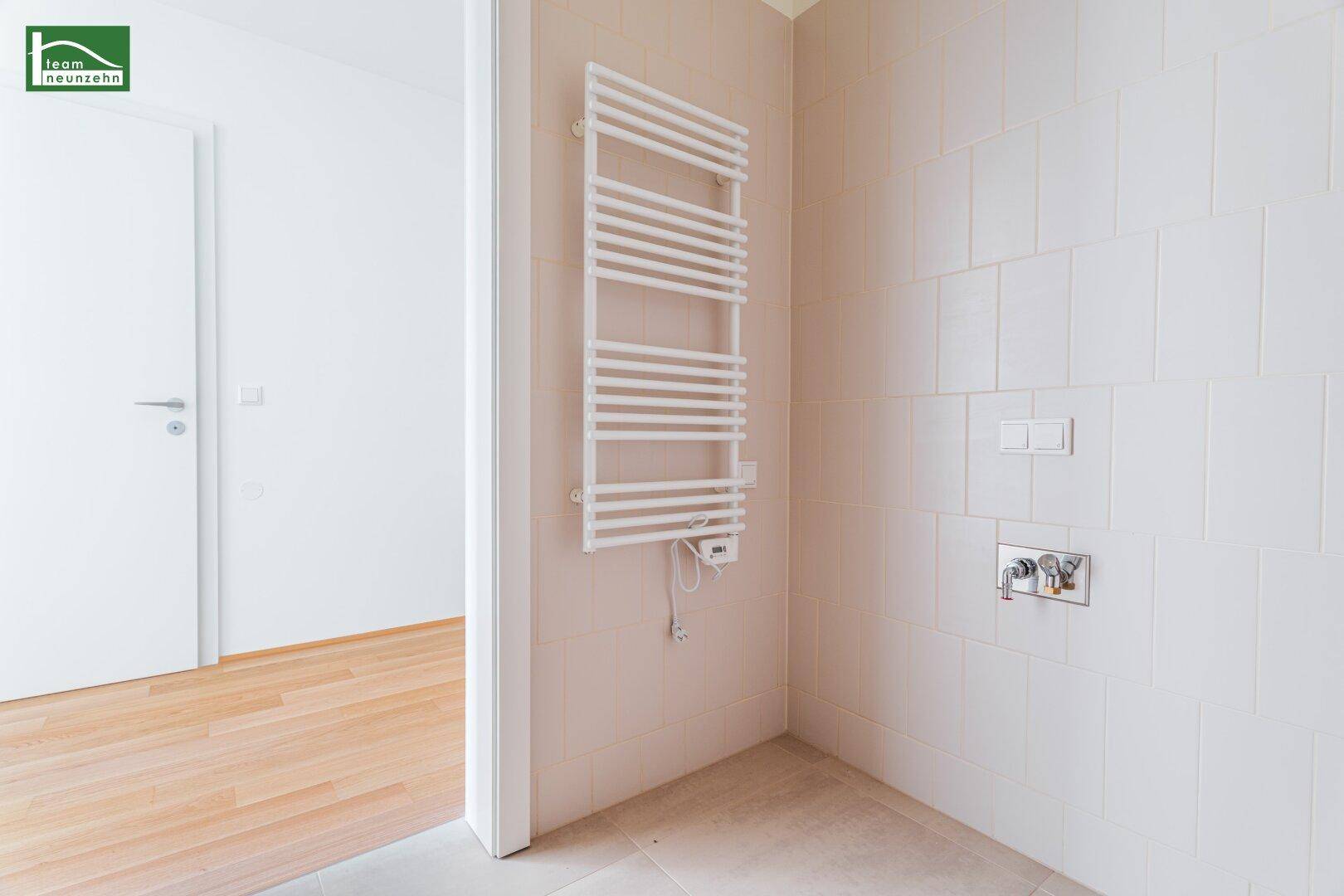 Badezimmer mit beheiztem Handtuchhalter und hellen Fliesen, bereit für die Installation einer Dusche.