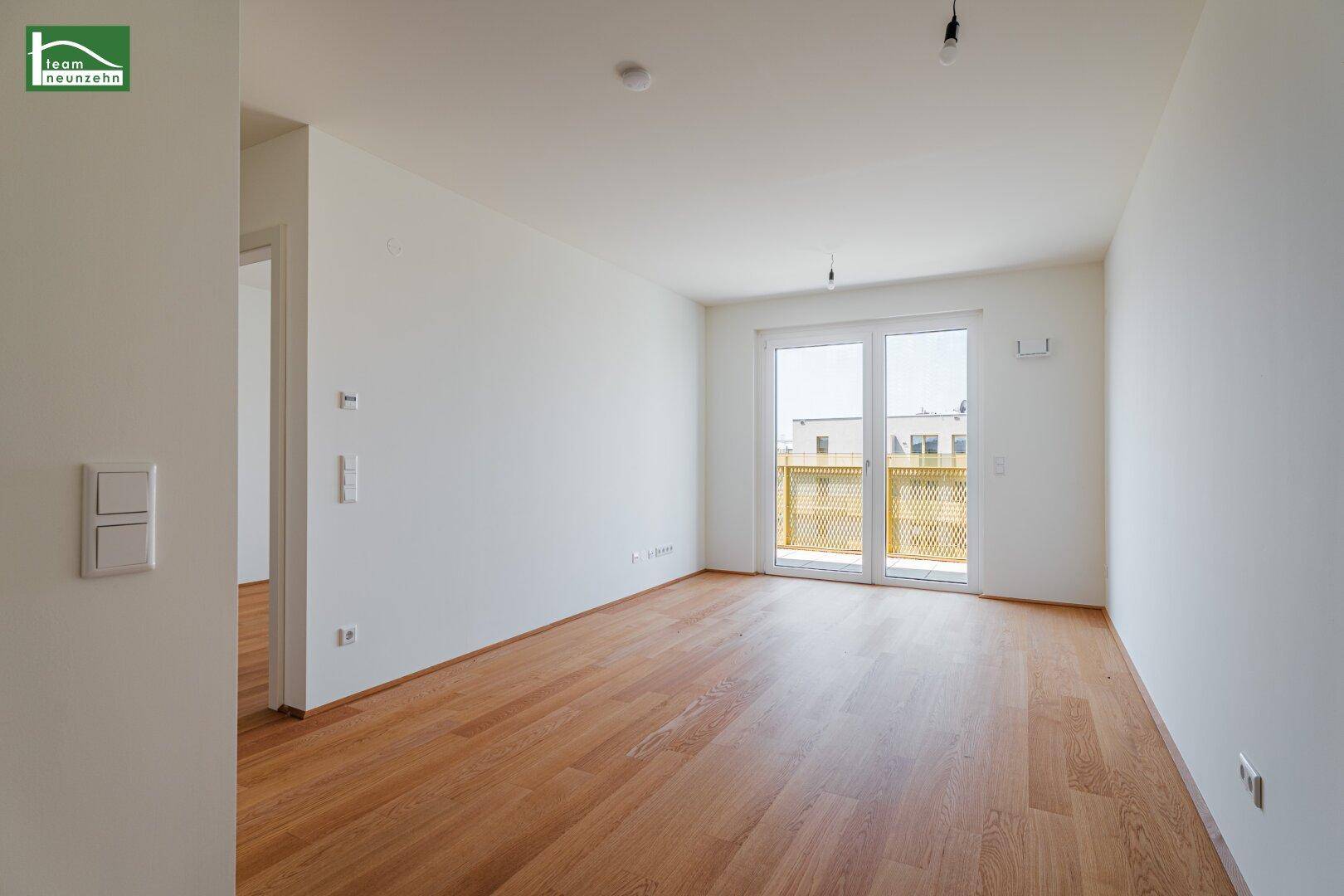 Geräumiges Zimmer mit Holzboden und großen Fenstern, die viel Tageslicht hereinlassen und Zugang zum Balkon bieten.