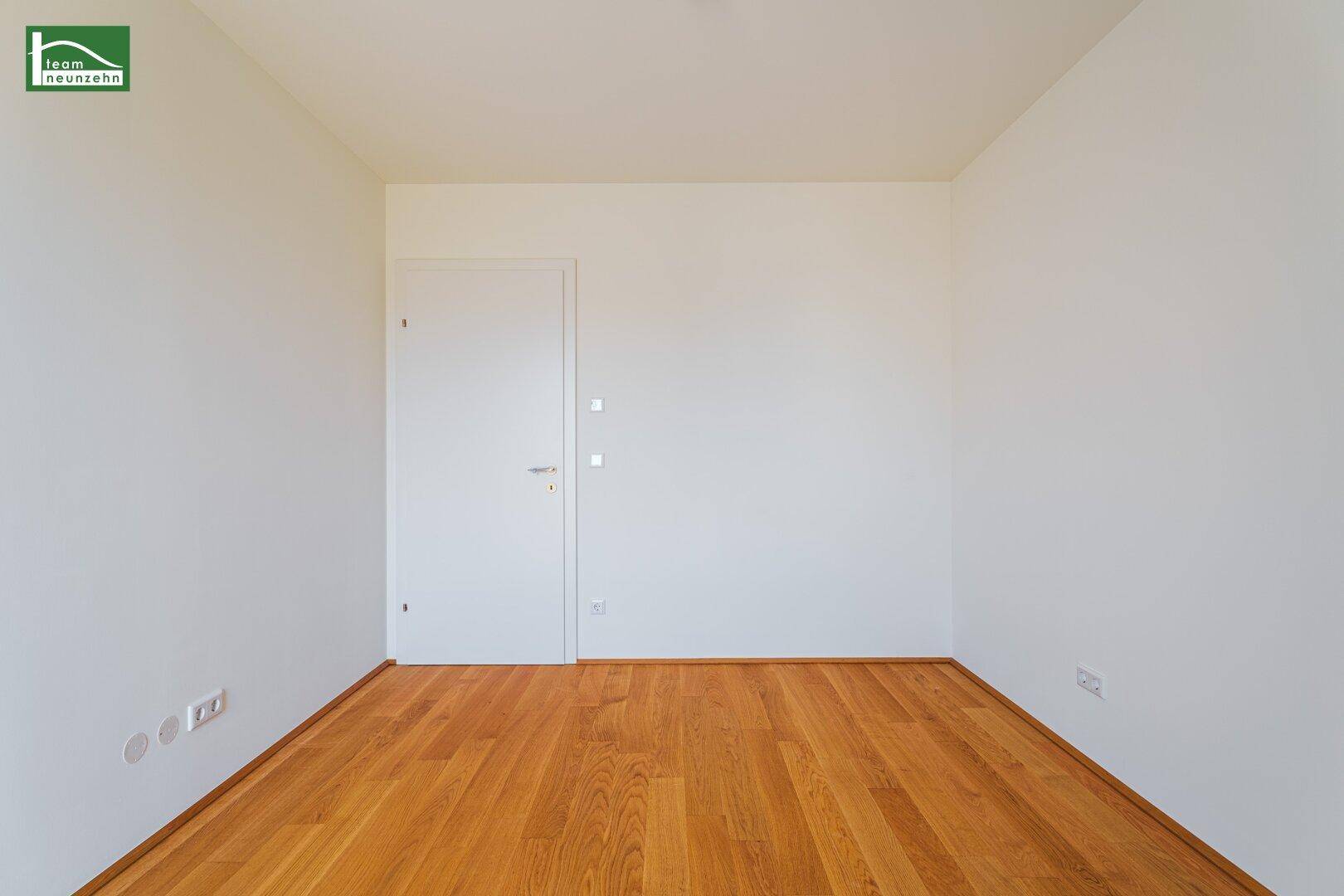 Leeres Zimmer mit hellem Holzboden und weiß gestrichenen Wänden, bereit zur Einrichtung.