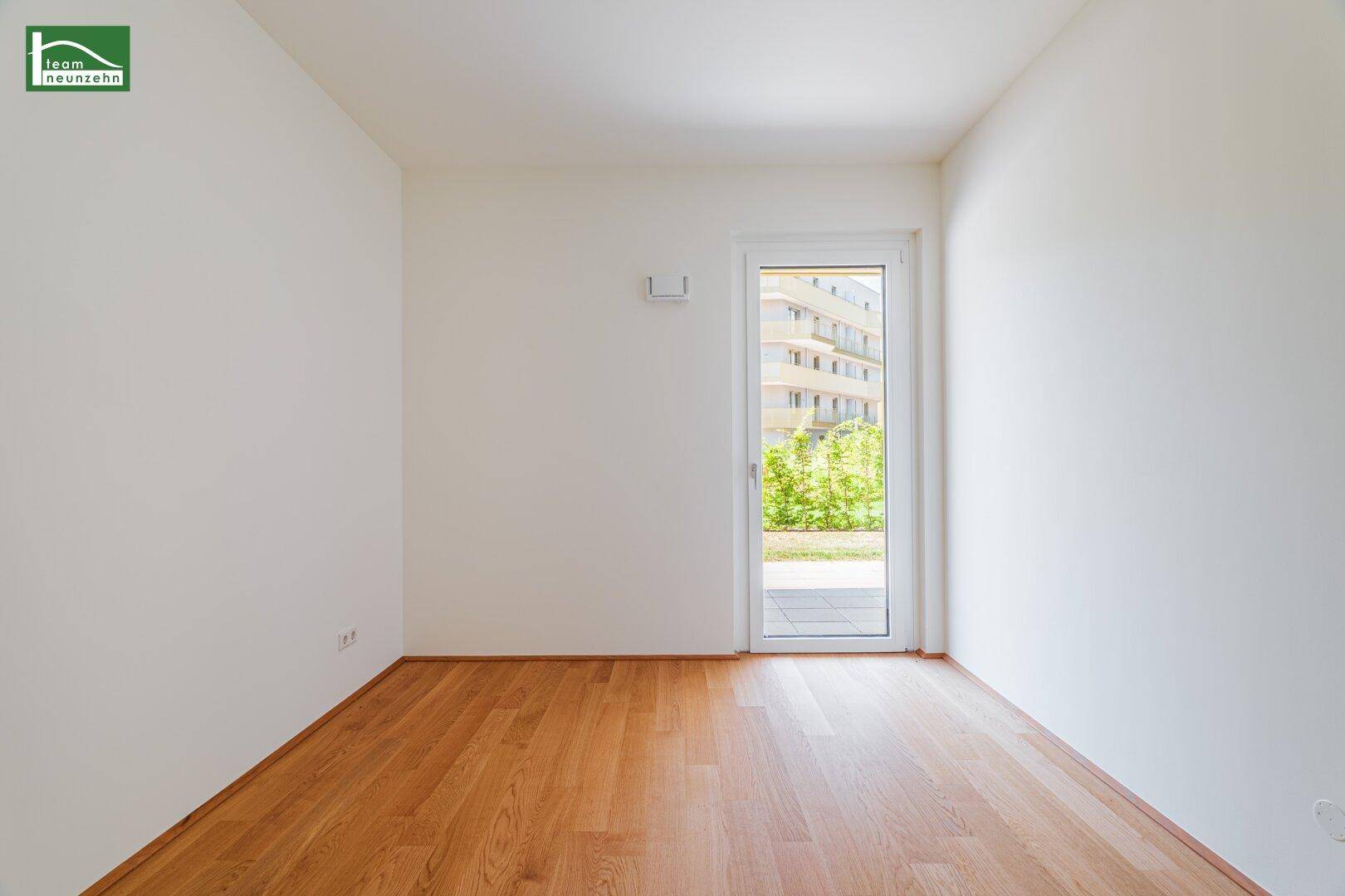 Leeres Schlafzimmer mit Holzboden und einer Tür, die direkten Zugang zum Gartenbereich bietet.