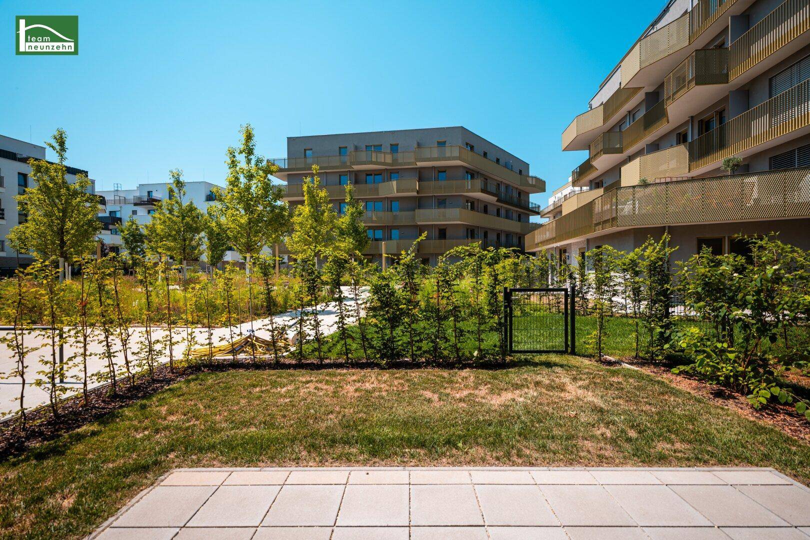 Weitläufige Gartenanlage mit Rasenflächen und Sträuchern, umgeben von modernen Wohngebäuden.
