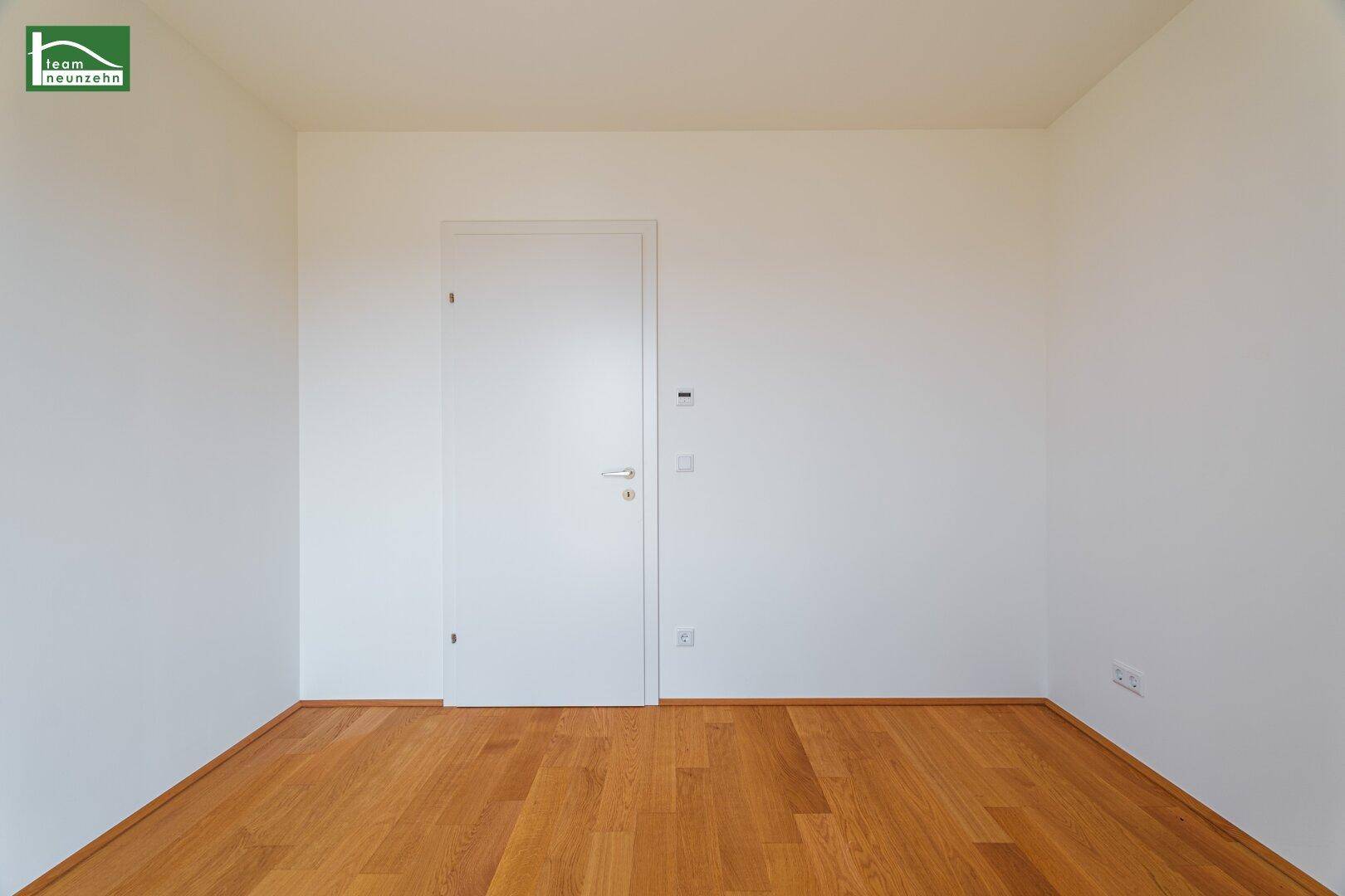 Leeres Zimmer mit Holzboden und weißer Tür, das vielseitig genutzt werden kann.