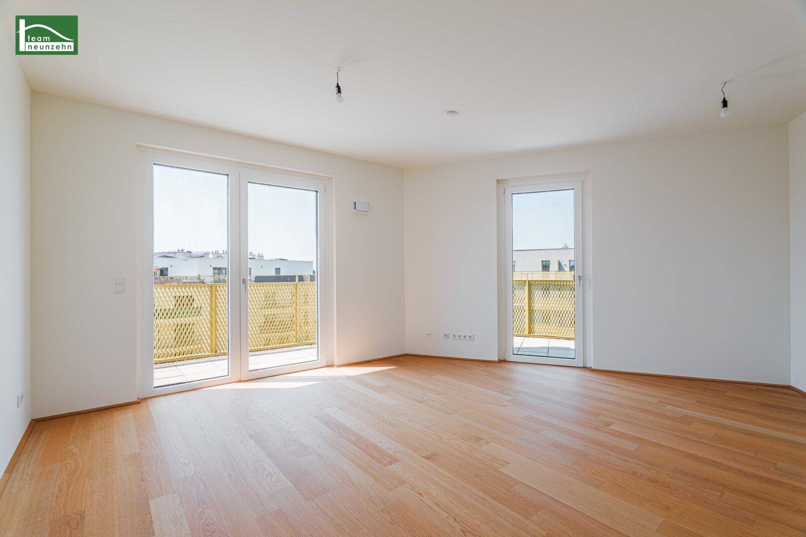 Geräumiges, helles Wohnzimmer mit Holzboden und mehreren Zugängen zu einem Balkon.