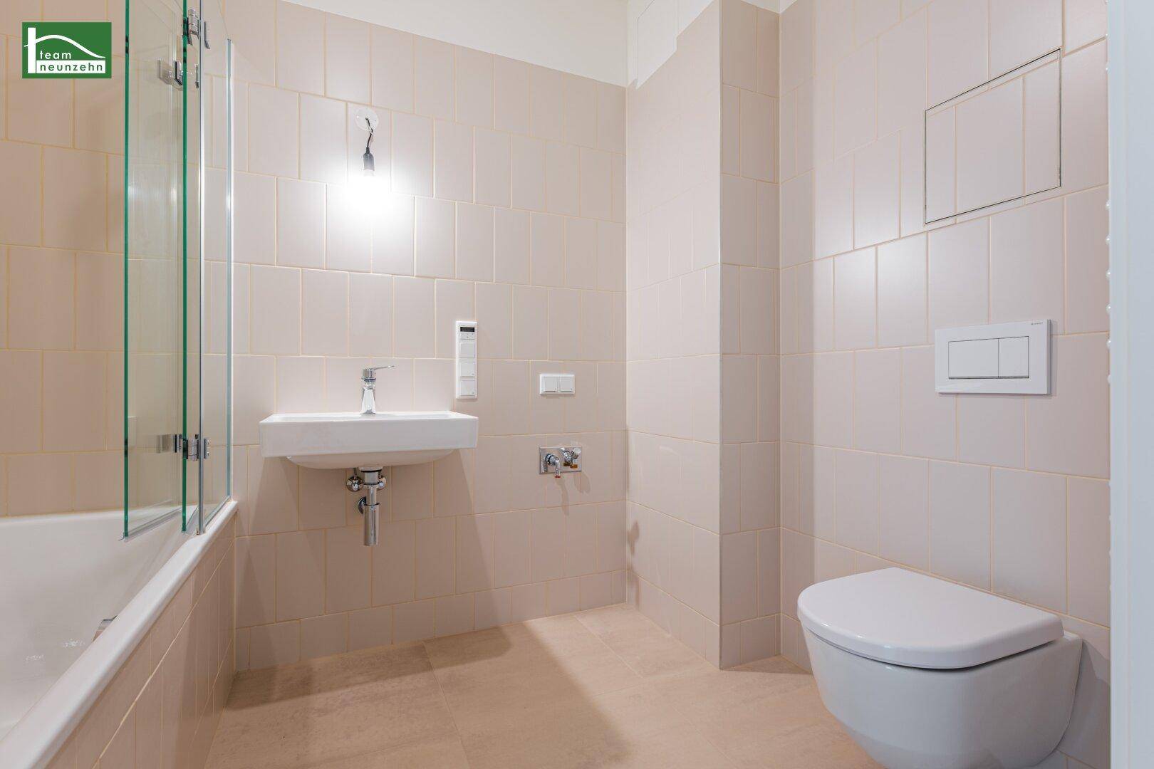 Modernes Badezimmer mit beigefarbenen Fliesen, Badewanne und wandhängendem WC.
