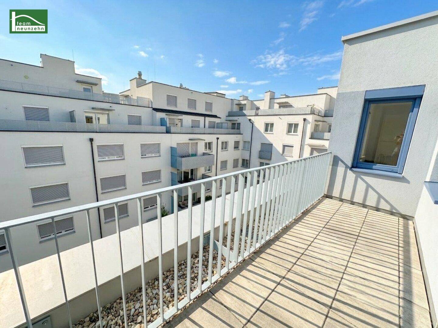 Großer Balkon mit Metallgeländer und Blick auf die umliegenden modernen Wohngebäude unter blauem Himmel.