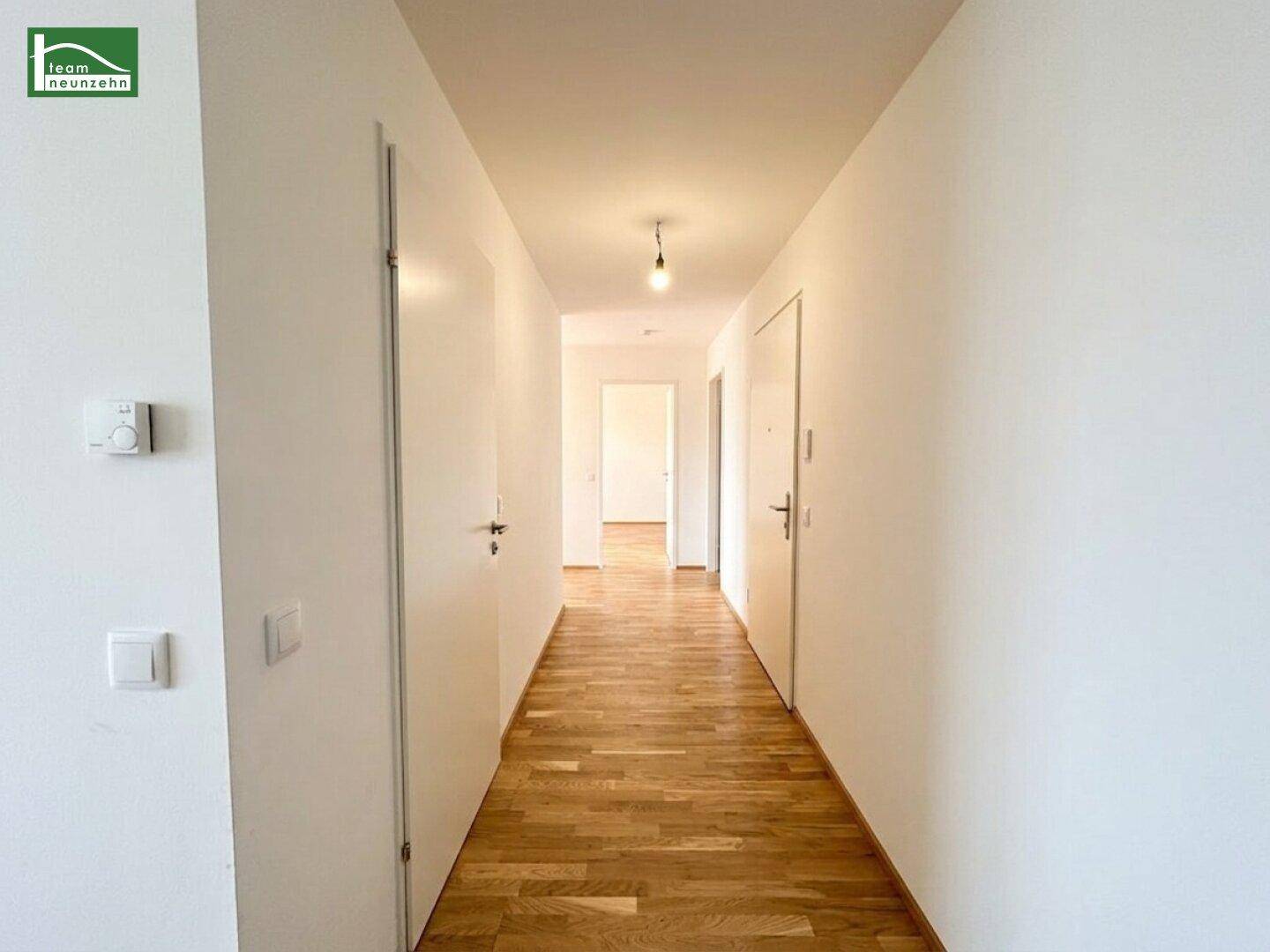 Langer, heller Flur mit Holzboden und weißen Wänden, der zu weiteren Räumen und Türen führt.