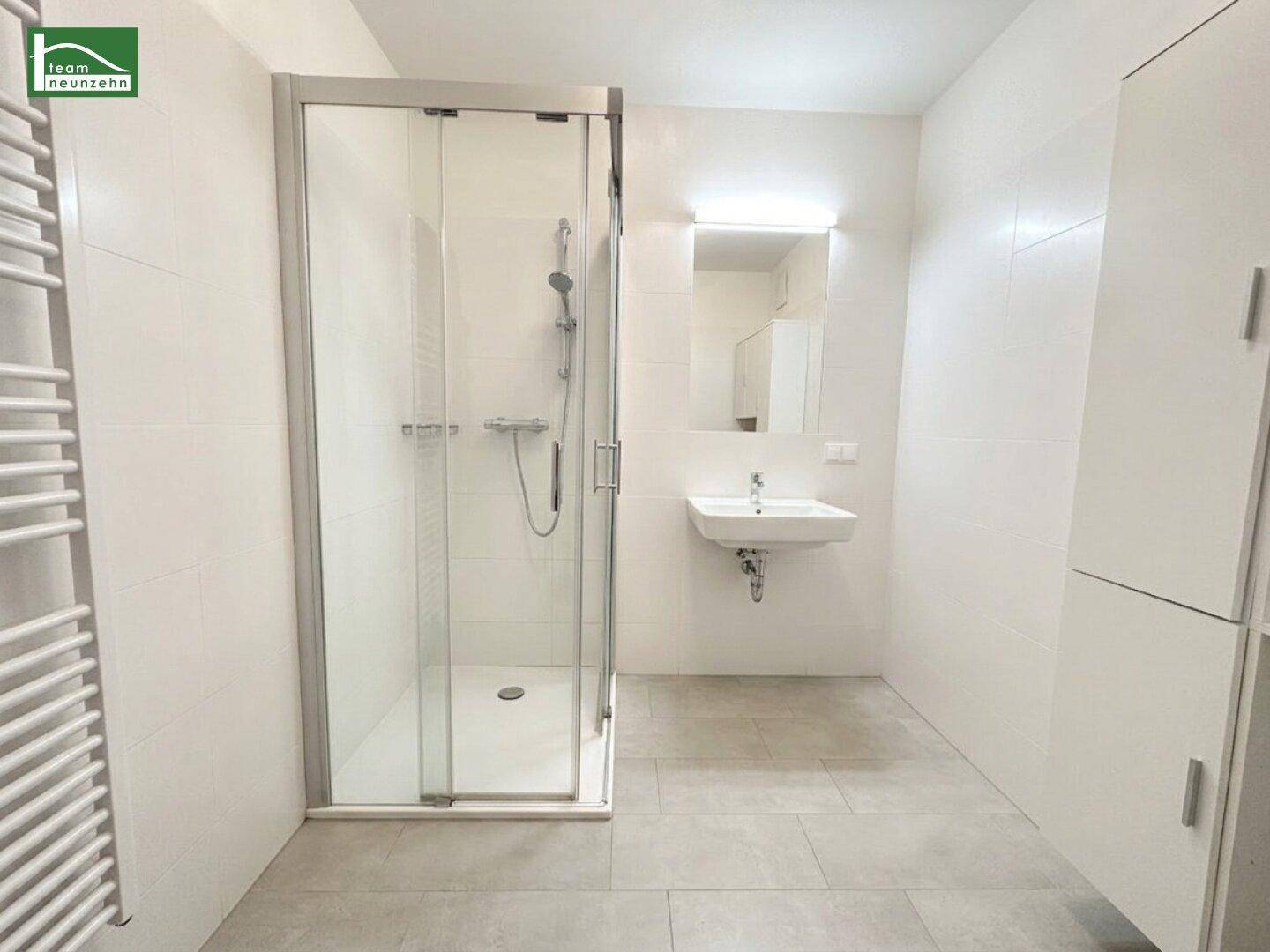 Modernes Badezimmer mit Duschkabine, Waschbecken, Spiegel und beheiztem Handtuchheizkörper an der Wand.