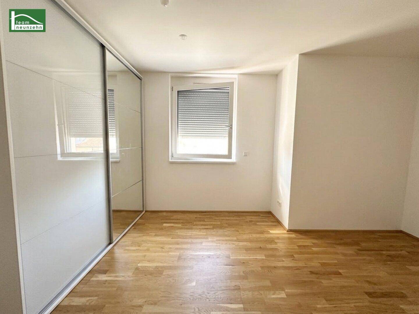 Schlafzimmer mit Holzboden, Fenster mit Rollladen und großem Spiegelschrank für viel Stauraum.