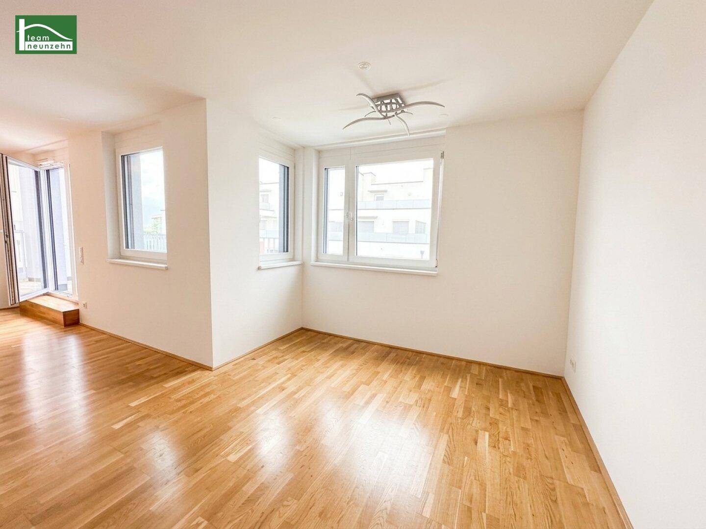 Heller Raum mit Holzboden und mehreren Fenstern, die eine gute Belichtung bieten und eine moderne Deckenleuchte.