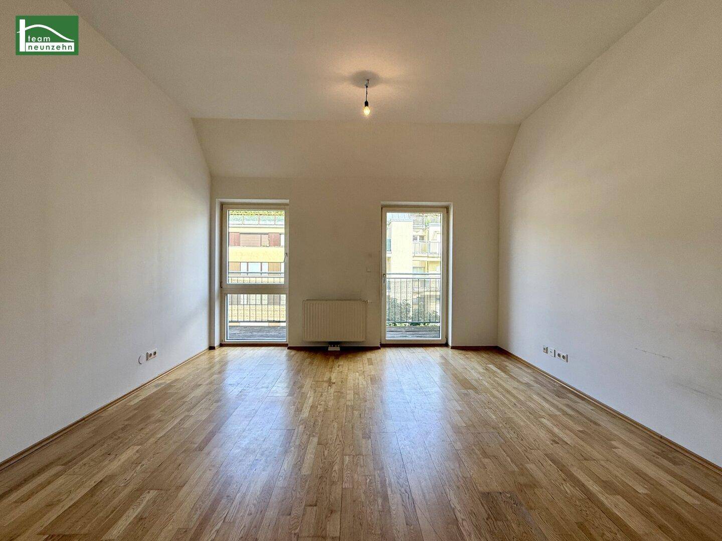 Heller Wohnraum mit Parkettboden, weißen Wänden und zwei französischen Balkonen.