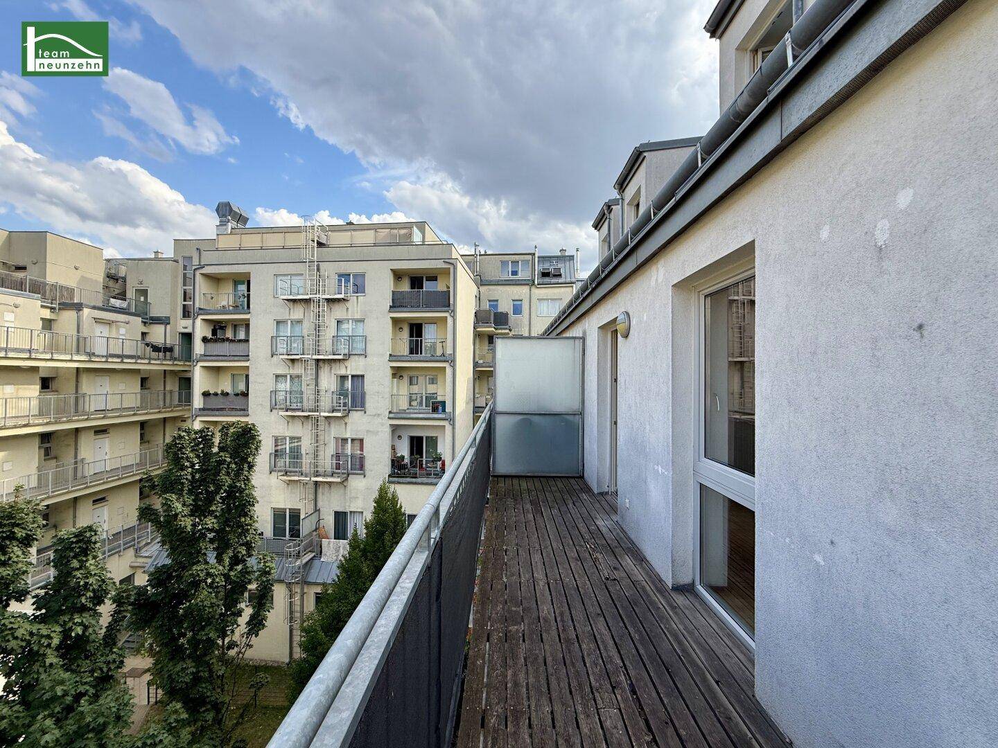 Langer Balkon mit Holzbelag und Blick auf umliegende Wohngebäude.
