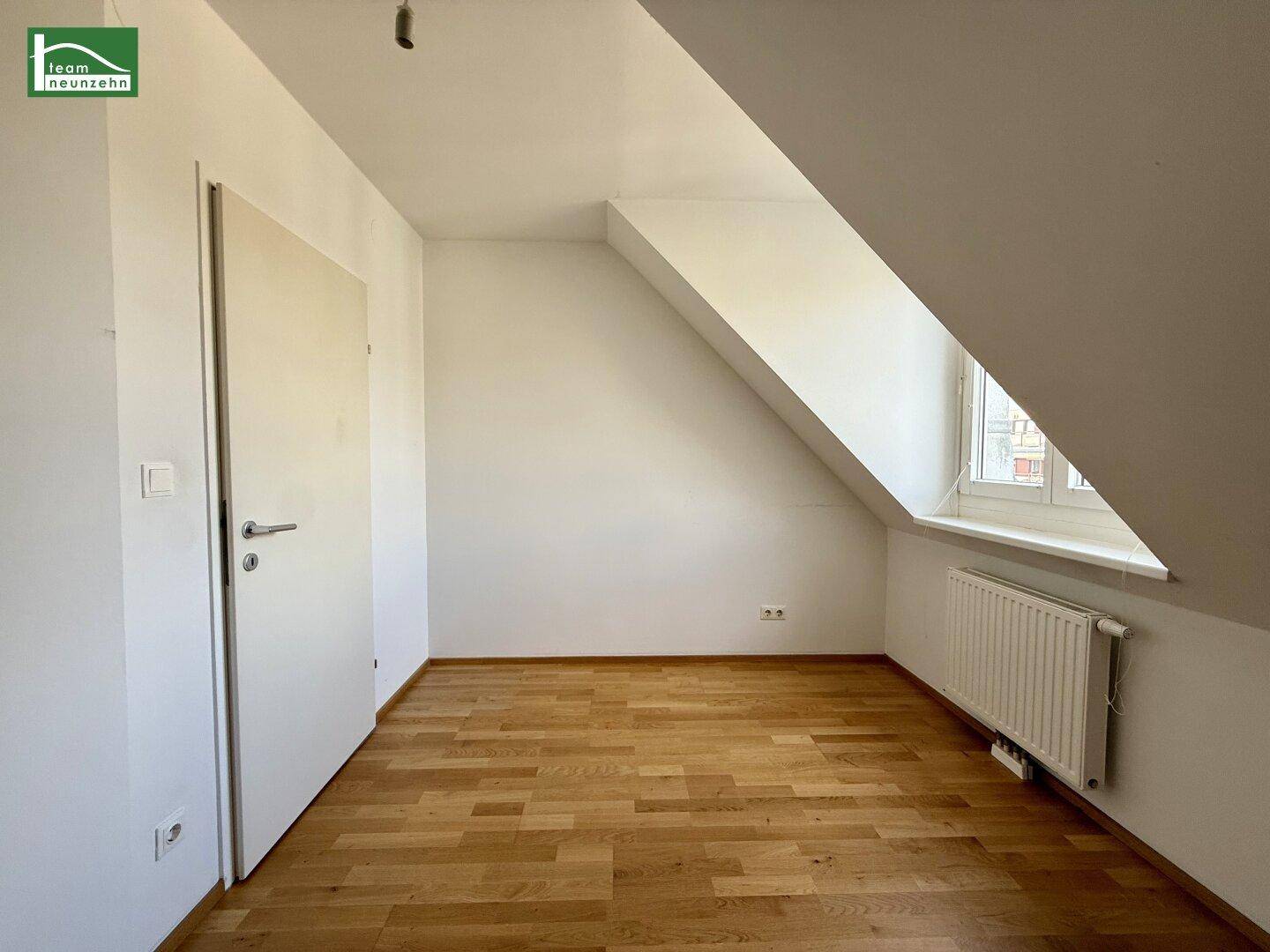 Dachgeschosszimmer mit Parkettboden, schrägen Wänden und Fenster.