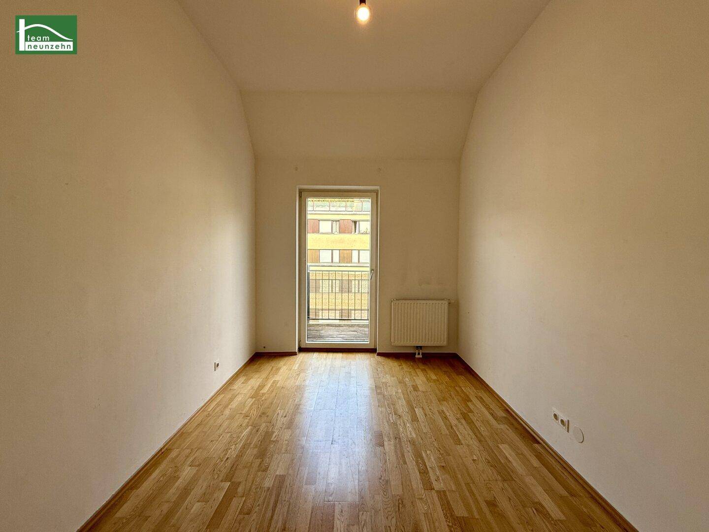 Helles Zimmer mit Parkettboden, weißen Wänden und Zugang zu einem französischen Balkon.