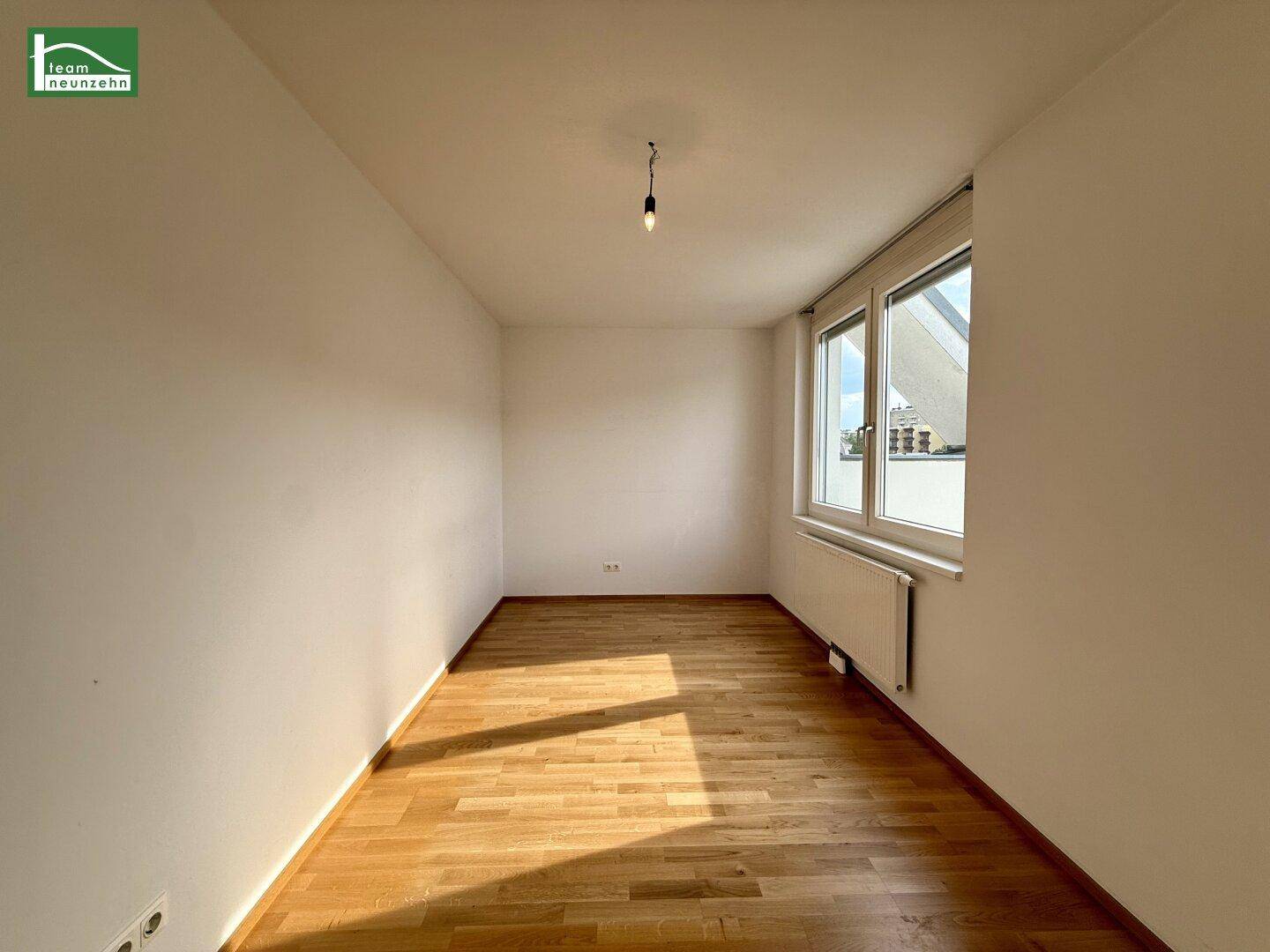 Helles Zimmer mit Parkettboden, weißen Wänden und großem Fenster.