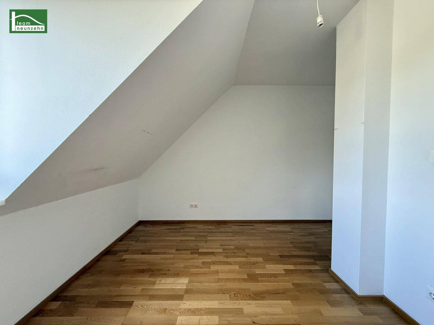 Leerer Dachbodenraum mit Parkettboden und schrägen Wänden.