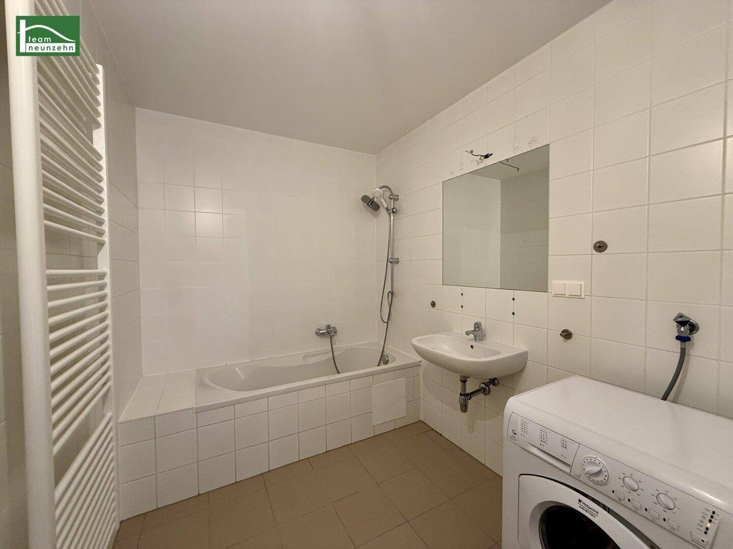 Badezimmer mit Badewanne, Dusche, Waschbecken, beheiztem Handtuchhalter und Waschmaschine.