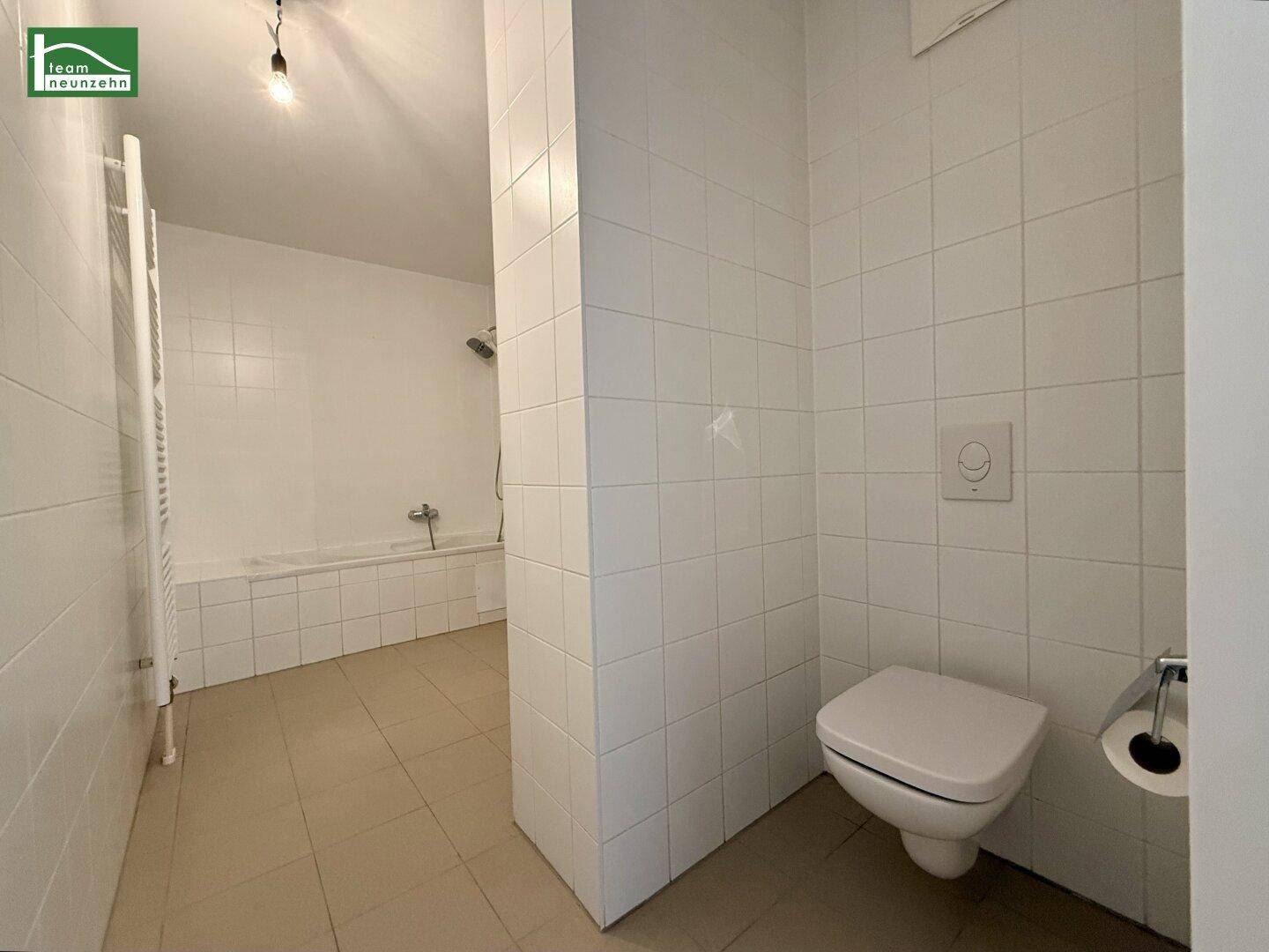 Badezimmer mit weißen Fliesen, wandhängendem WC und Blick auf den Duschbereich.