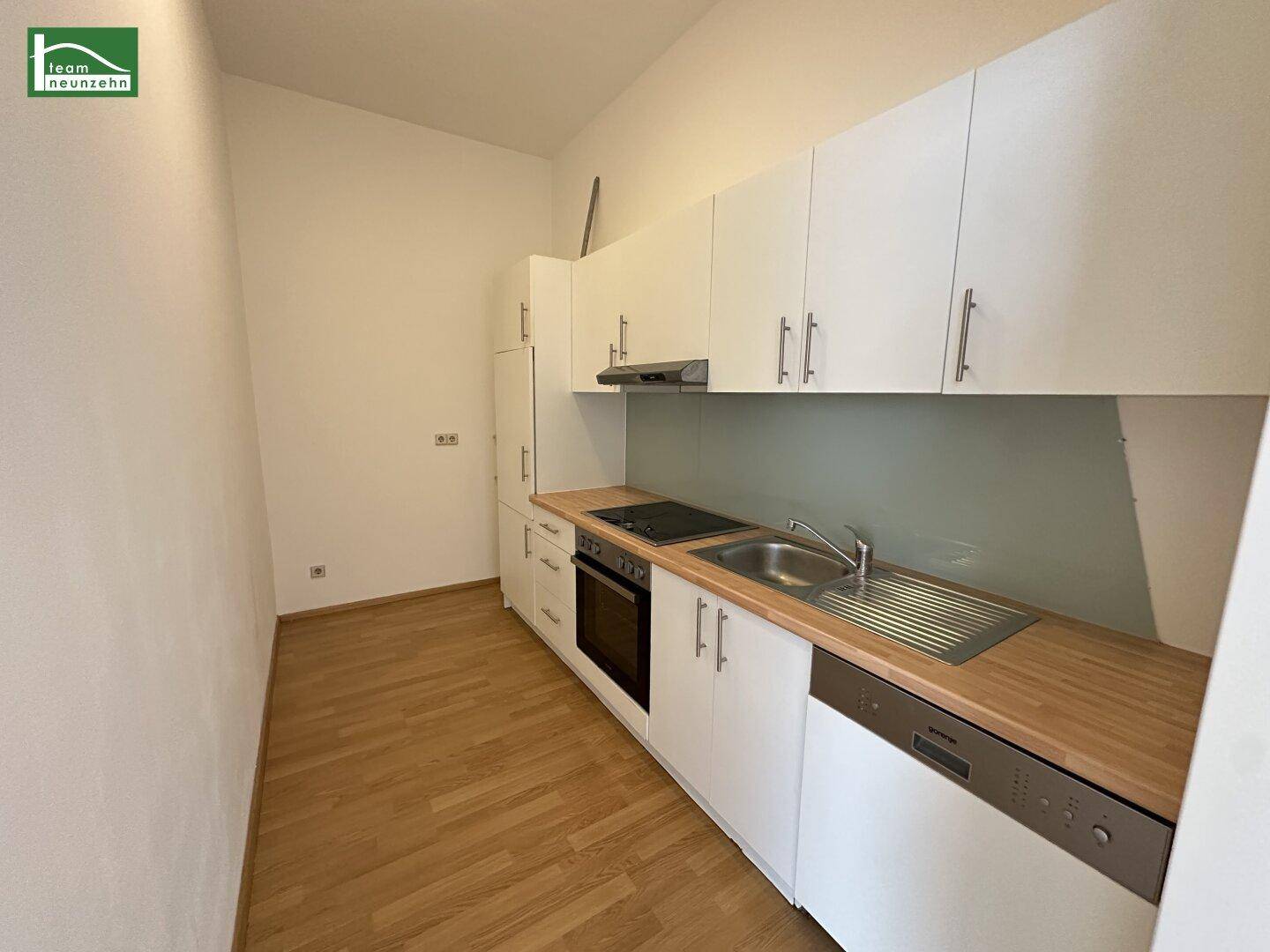 Funktionale Einbauküche mit weißen Schränken, Holz-Arbeitsplatte und integrierten Geräten.
