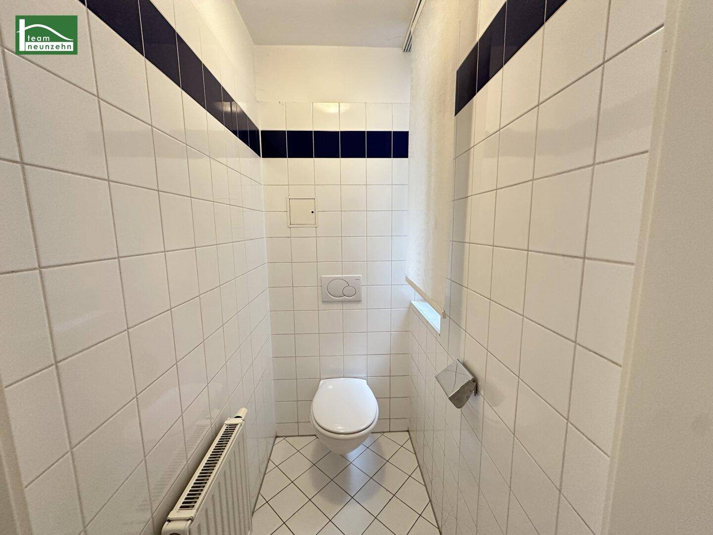Separate Toilette mit weißen Fliesen, Wand-WC und Heizkörper.