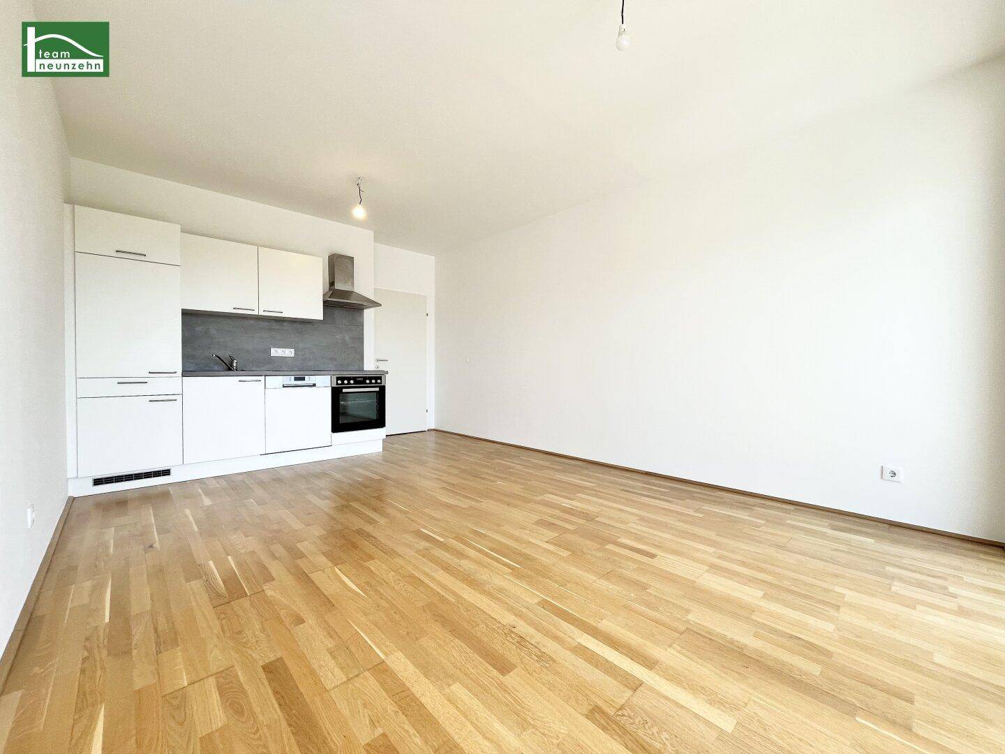 Offener Wohn- und Essbereich mit integrierter Einbauküche und hellem Parkettboden.