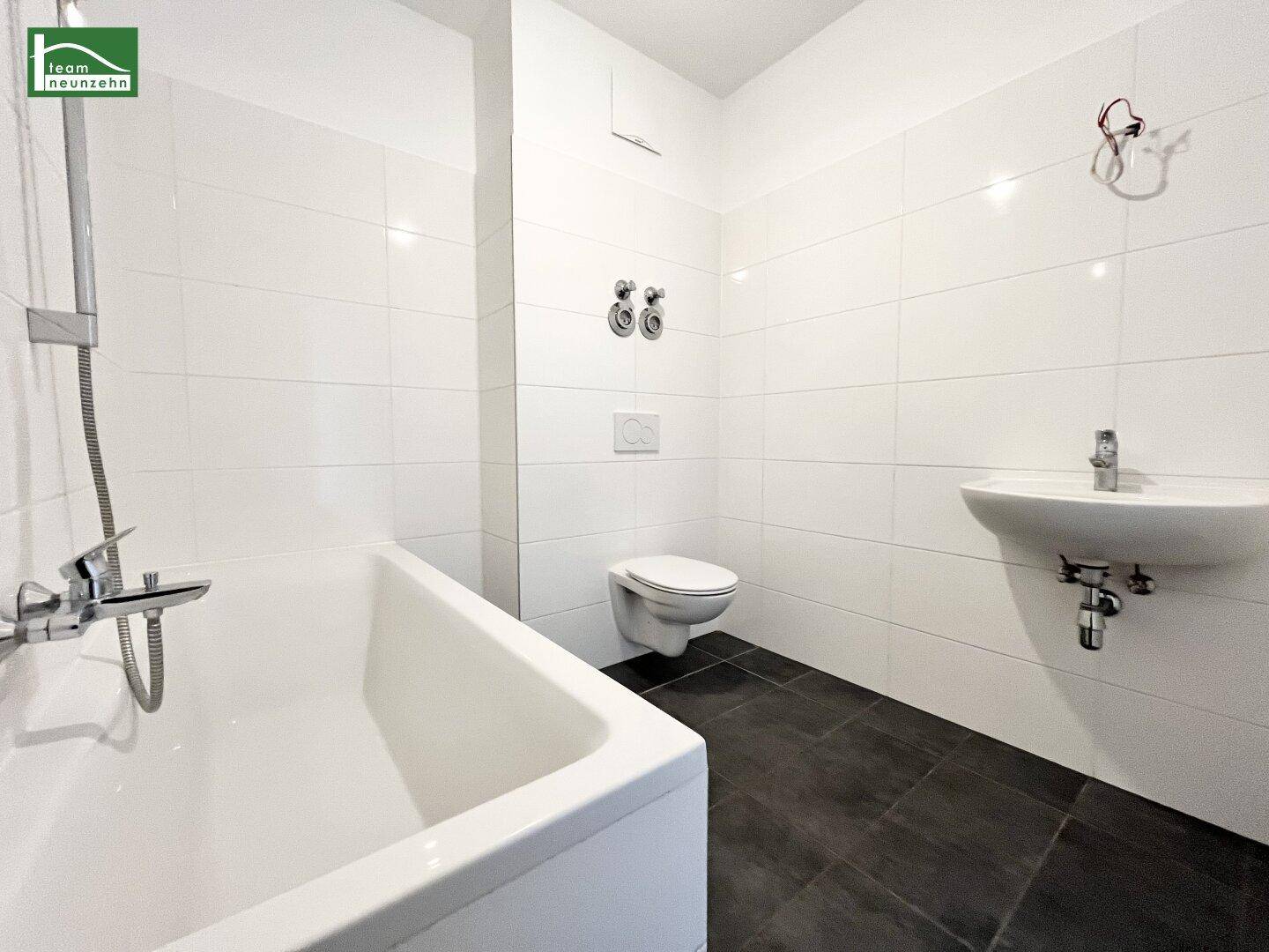 Modernes Badezimmer mit weißen Fliesen, dunklem Boden und integrierter Badewanne und WC.