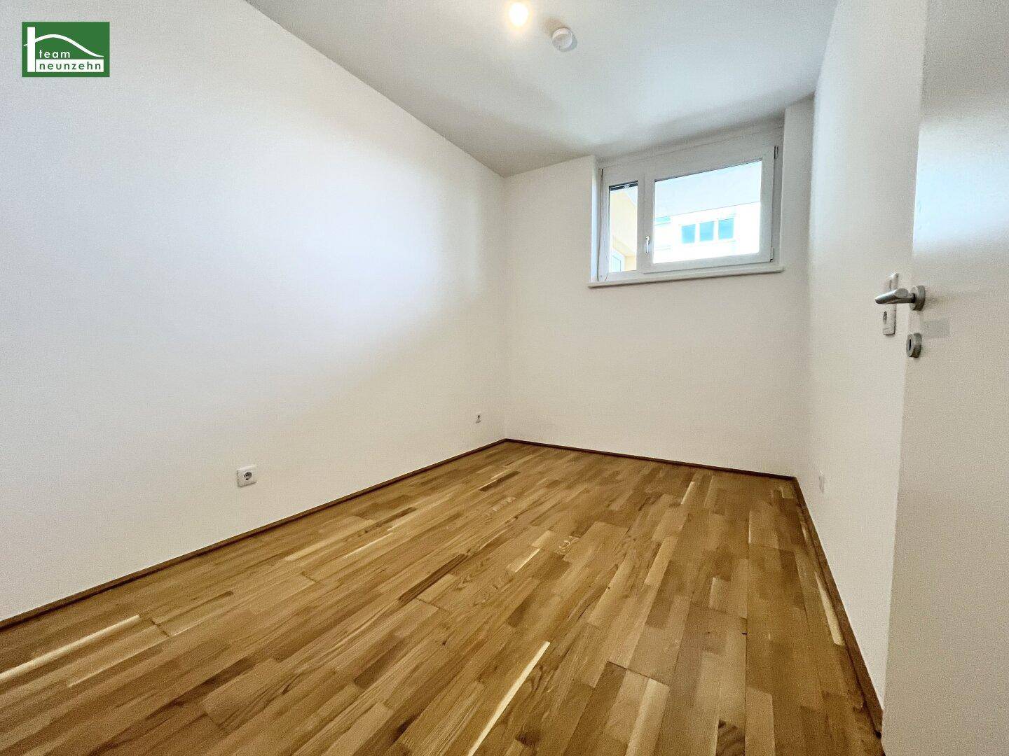 Helles, unmöbliertes Zimmer mit Parkettboden und einem Fenster, das Tageslicht hereinlässt.
