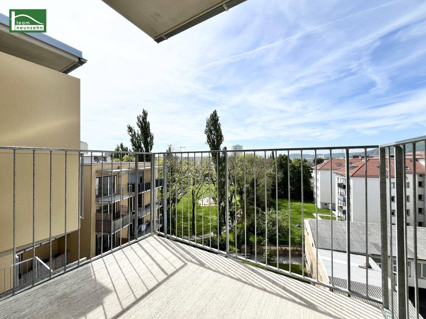 Geräumiger Balkon mit Metallgeländer und Blick auf grüne Bäume und die Umgebung.