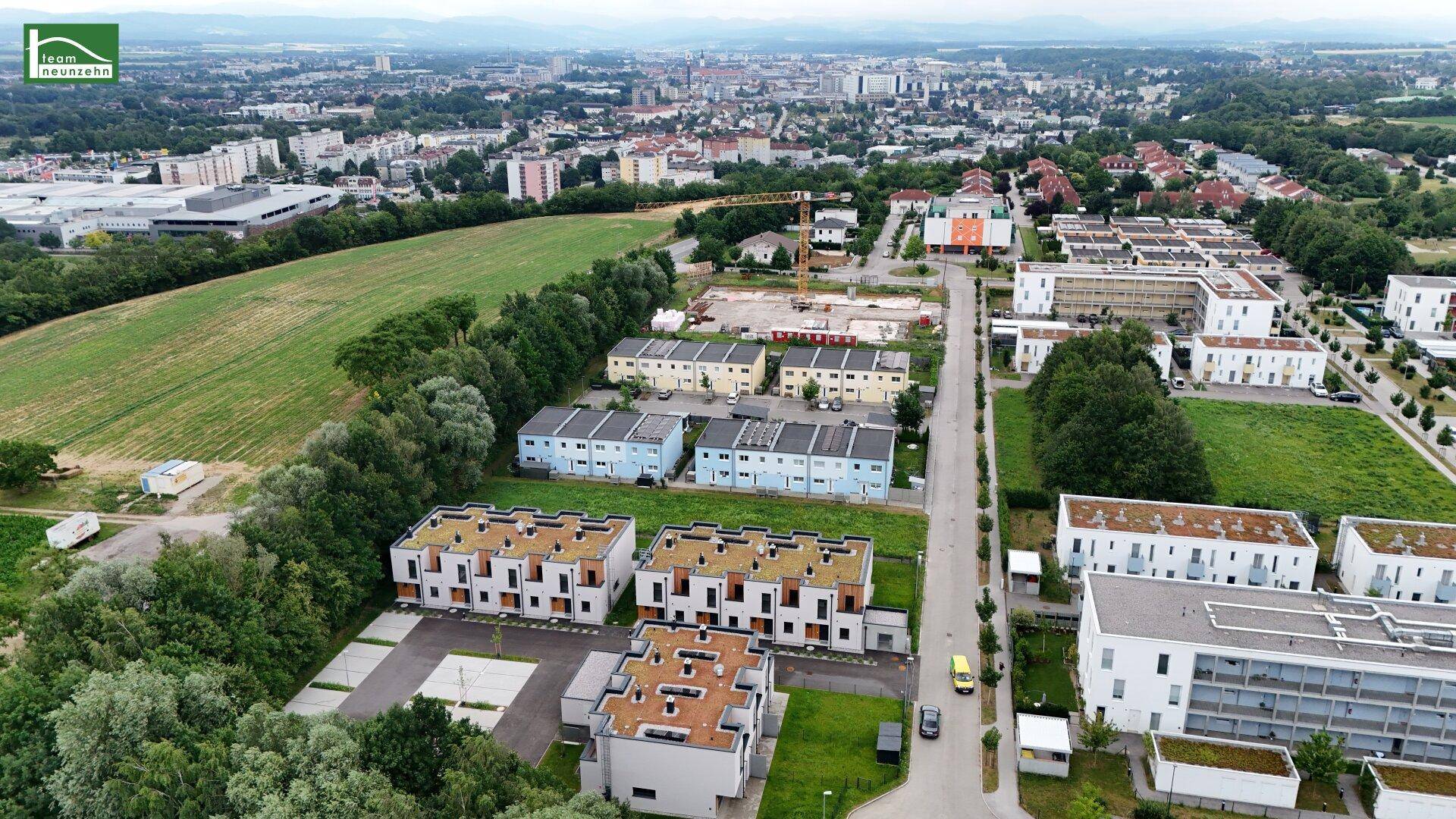 Luftaufnahme einer gemischten Wohnbebauung mit Neubauten, Grünflächen und Blick auf die Stadt.