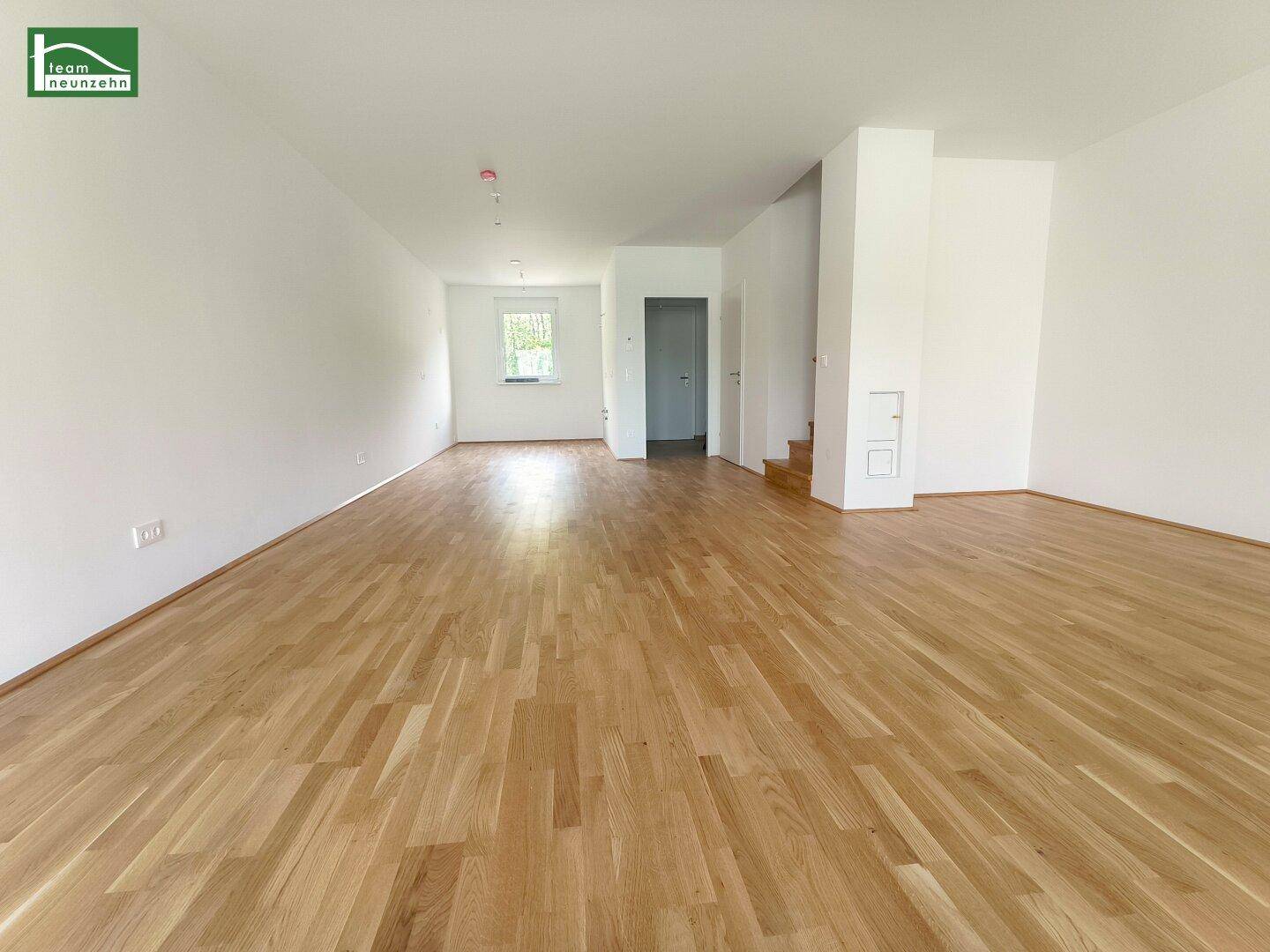 Lichtdurchfluteter, offener Wohnbereich mit Holzparkettboden und Zugang zu weiteren Räumen.